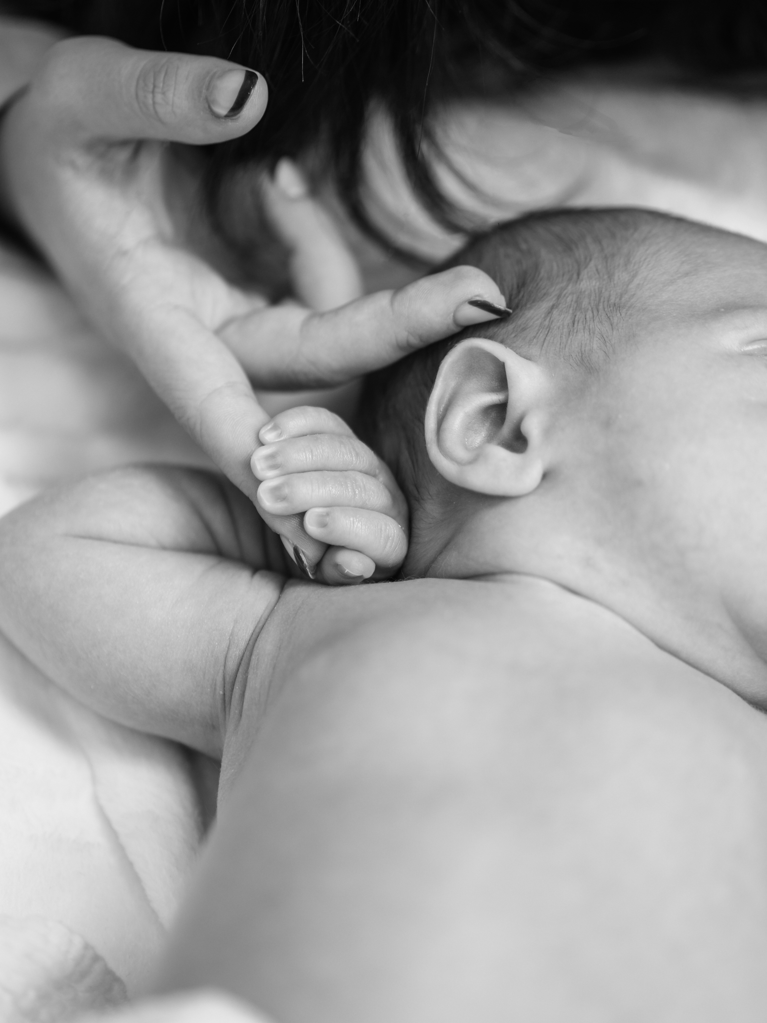 Close-up of a mother breastfeeding her baby, with the baby's head resting on the mother's chest, in black and white.