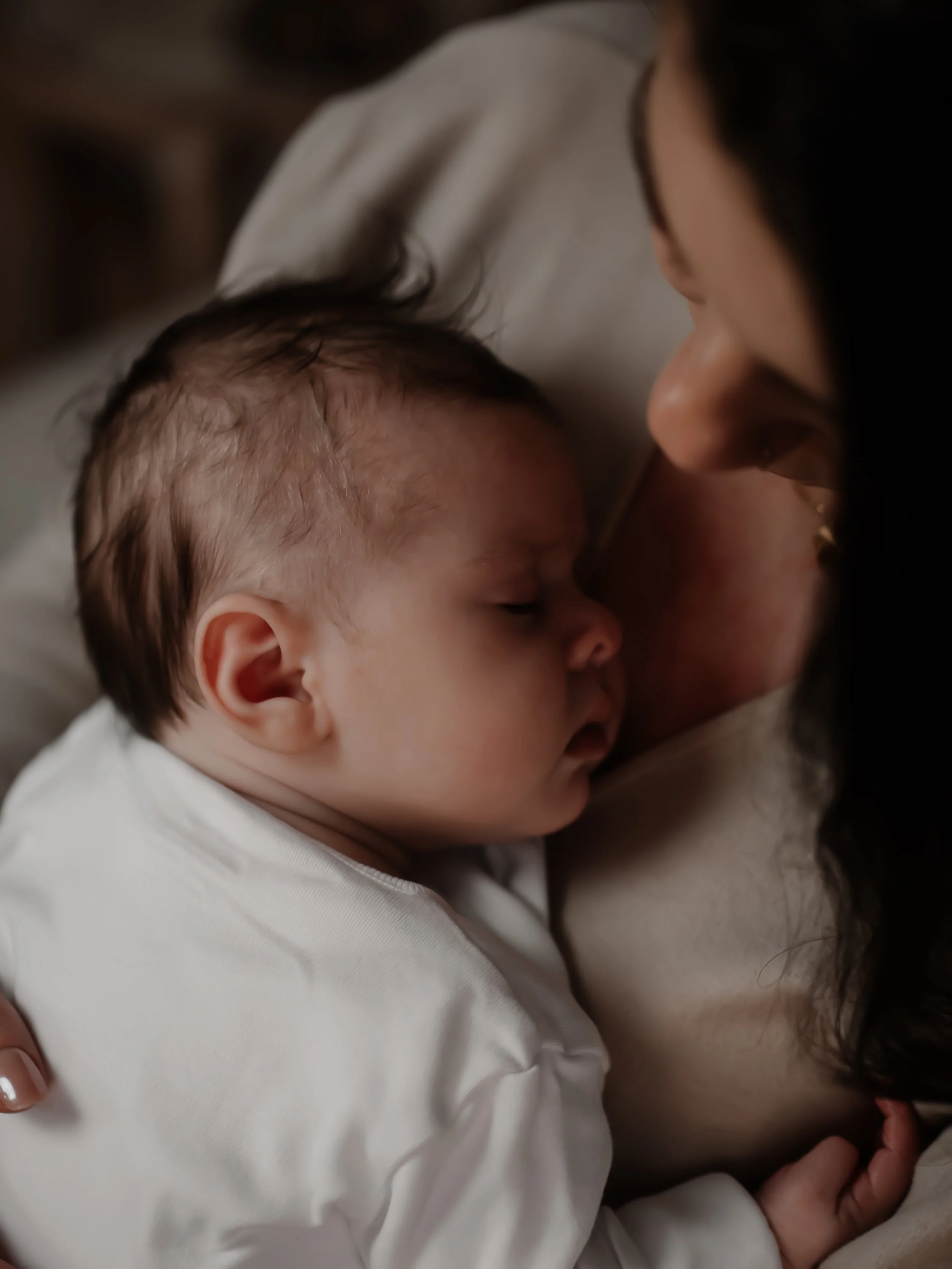 A baby sleeping peacefully on a woman's chest, with both of them resting close together.