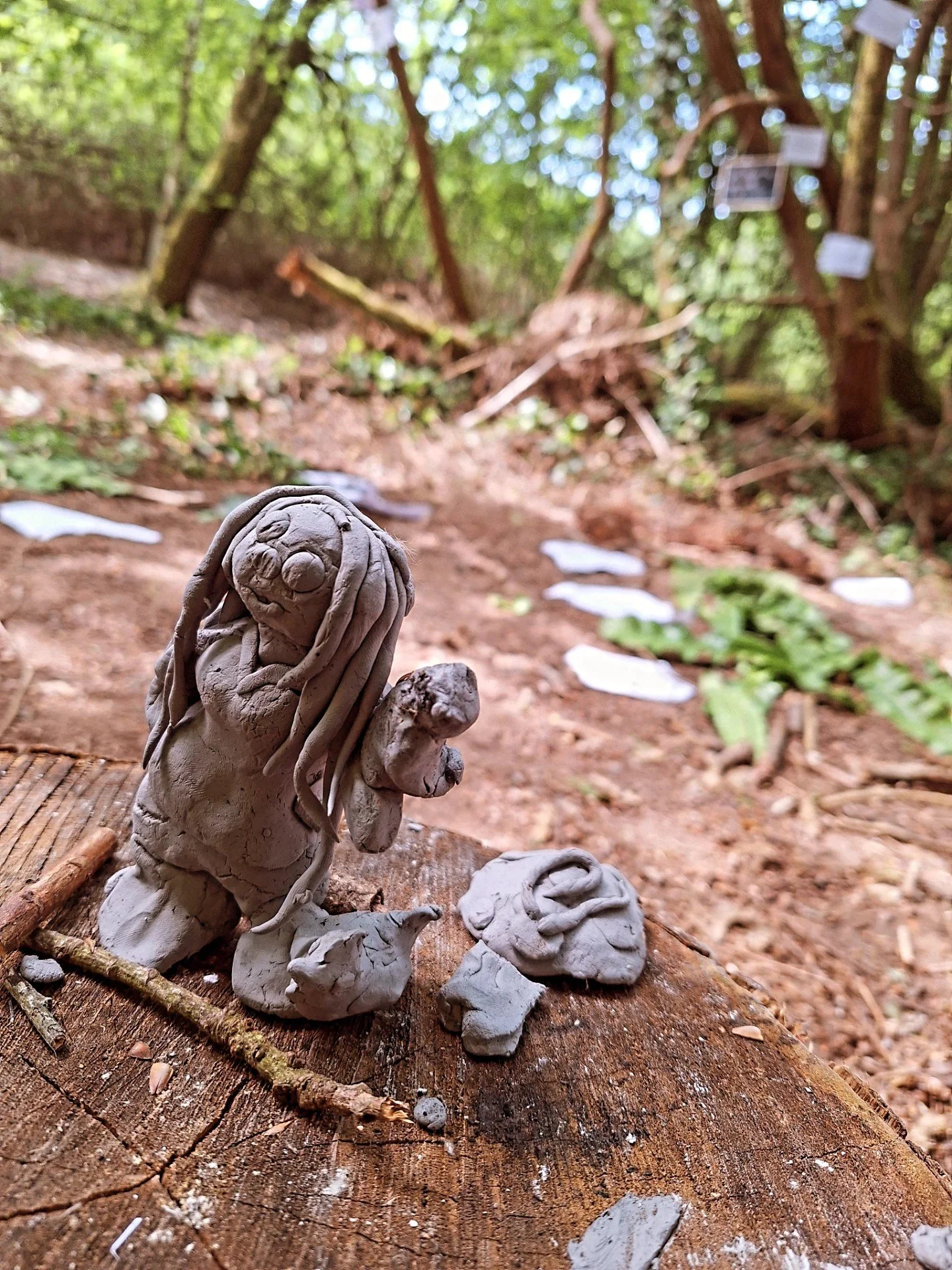 Clay sculptures of animals on a tree trunk in a wooded outdoor setting.