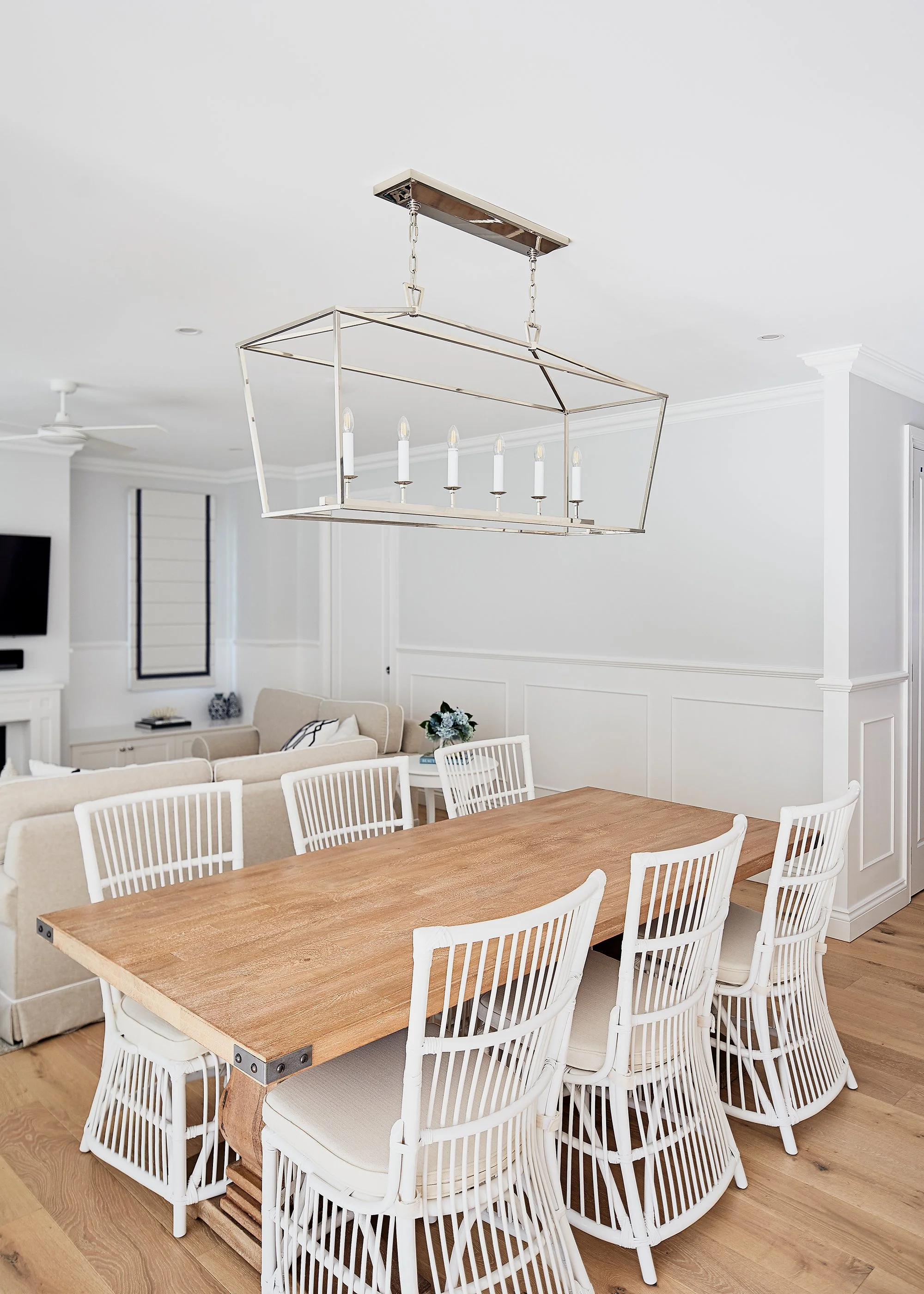 A modern dining room with a wooden table, white chairs, and a chandelier with candle-shaped lights overhead.