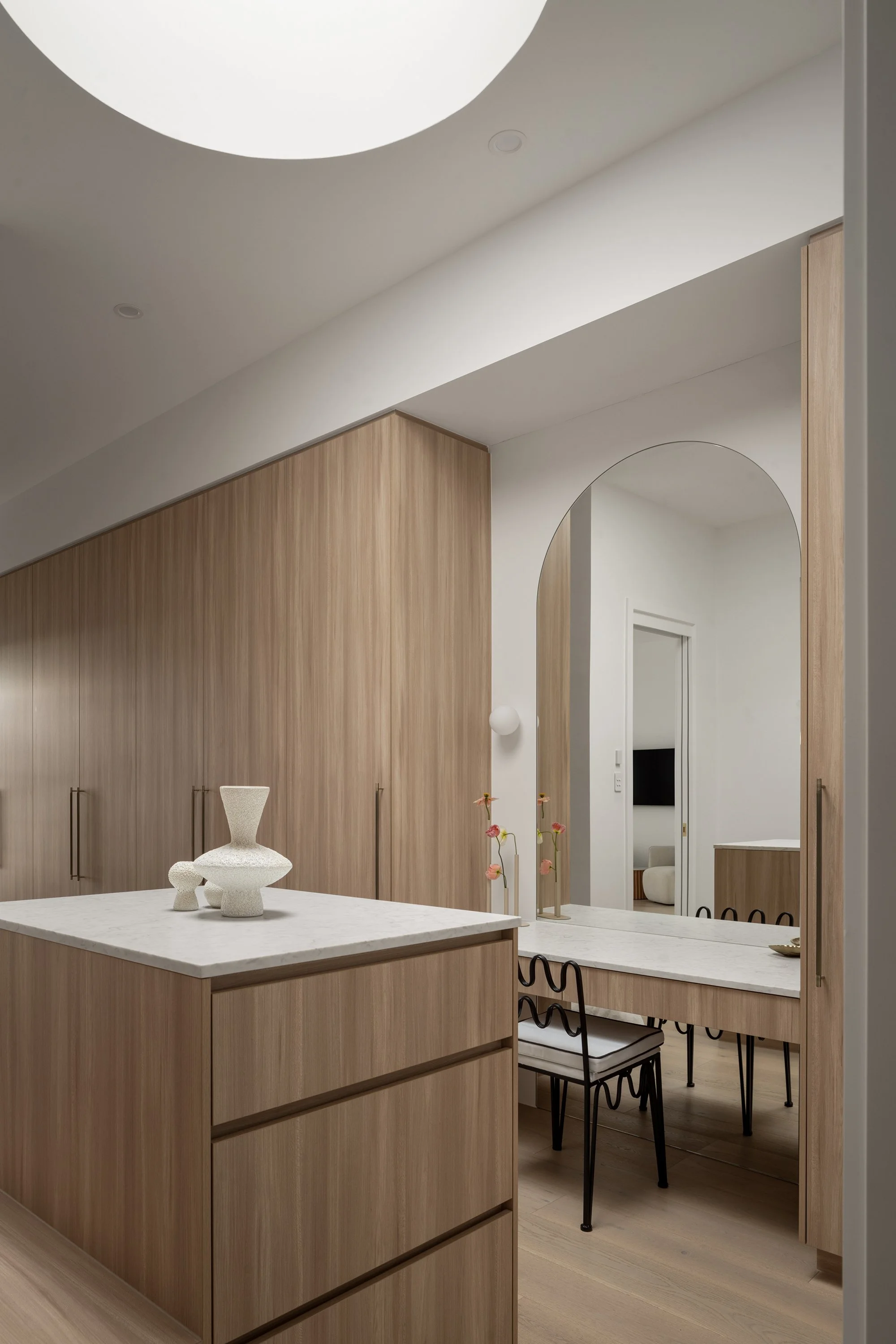 Modern kitchen and dining area with light wood cabinetry and a white marble island, minimalist decor, and a mirror reflecting a doorway.