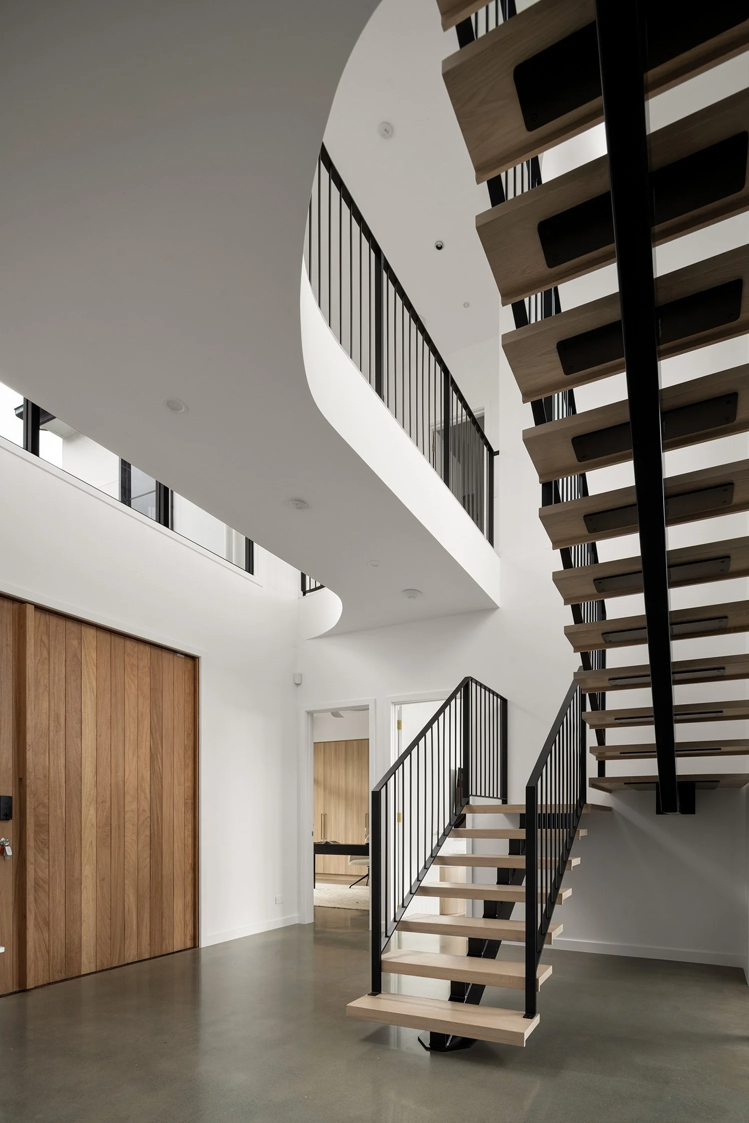 Interior view of a modern staircase with wooden steps and black metal railings in a minimalist home.