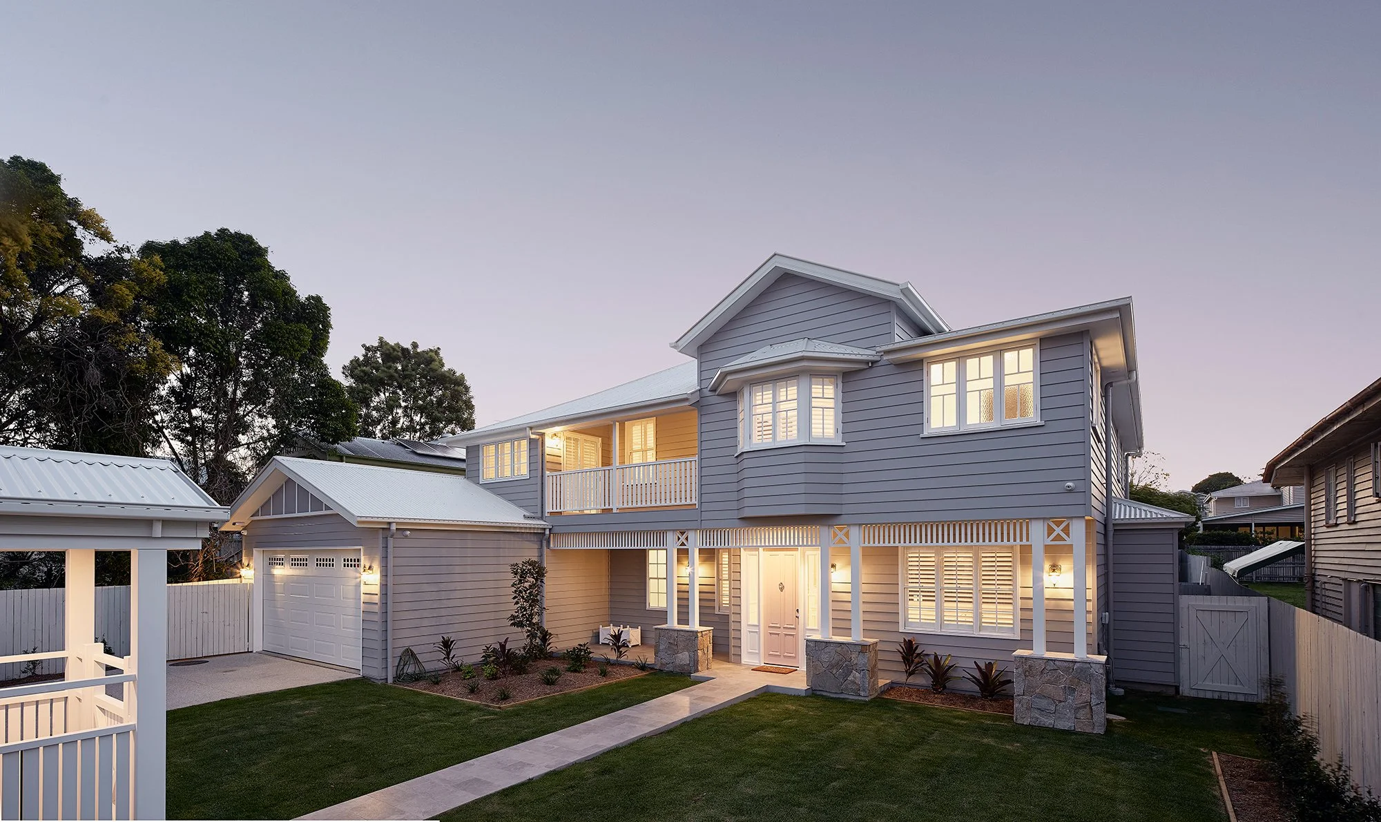 Exterior view of a two-story house with blue siding, lit windows, and a front porch, during dusk.