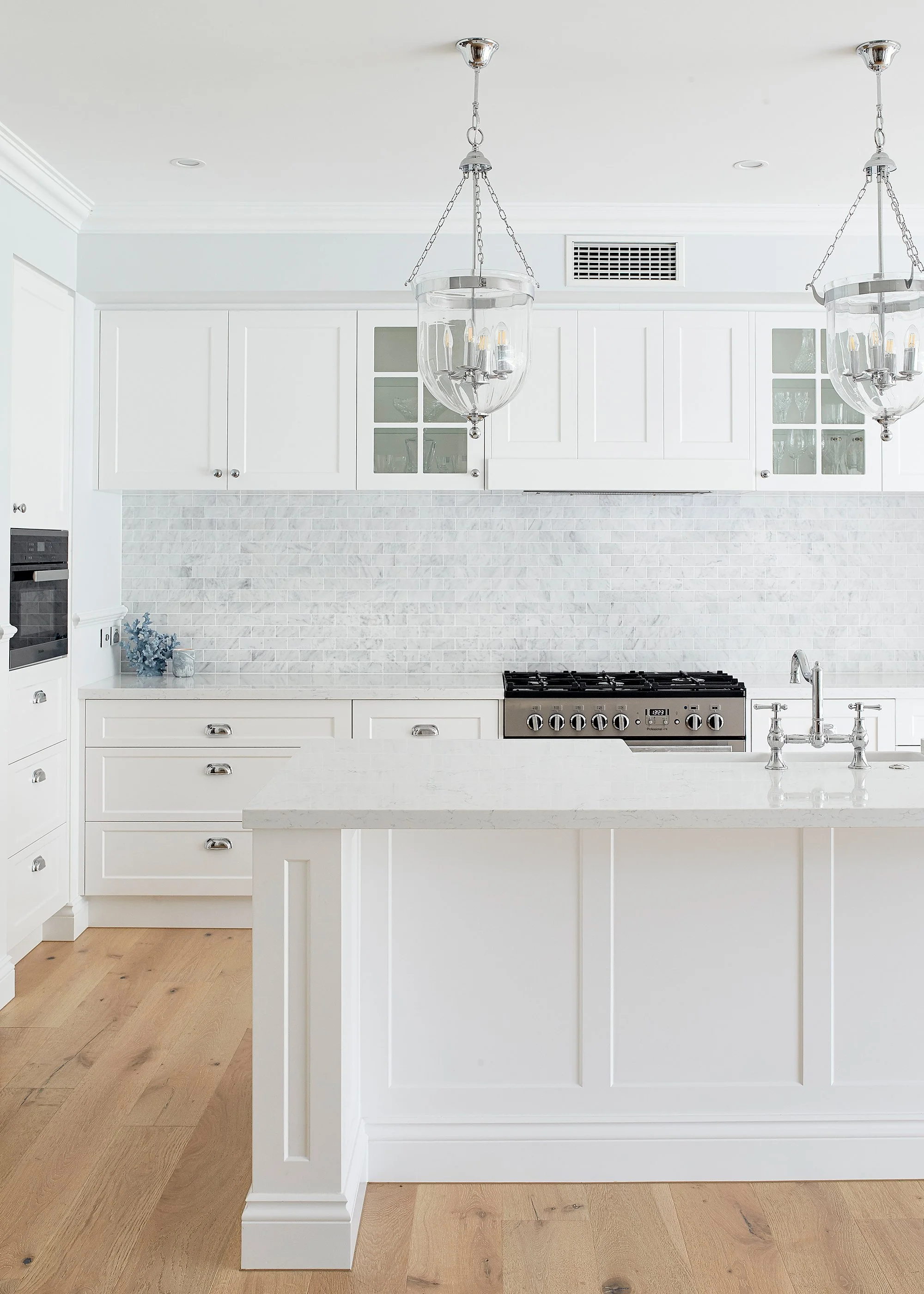 White kitchen with white cabinets, a white island with a marble countertop, stainless steel appliances, and two pendant lights hanging from the ceiling.