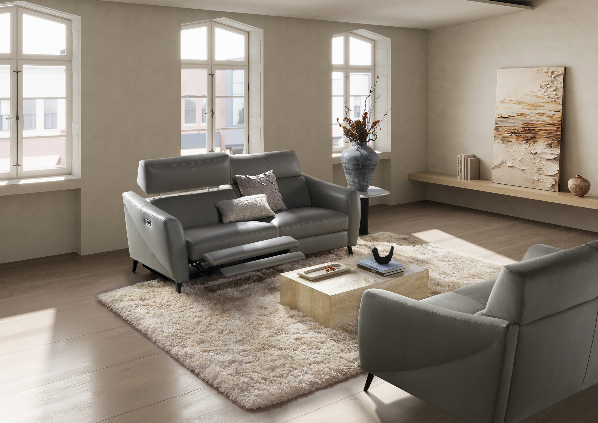 A modern living room with four large windows, two white leather armchairs, a beige shaggy rug, a light-colored wooden coffee table with books and decor, a tall vase with dried branches, and a large abstract painting on a wooden shelf.