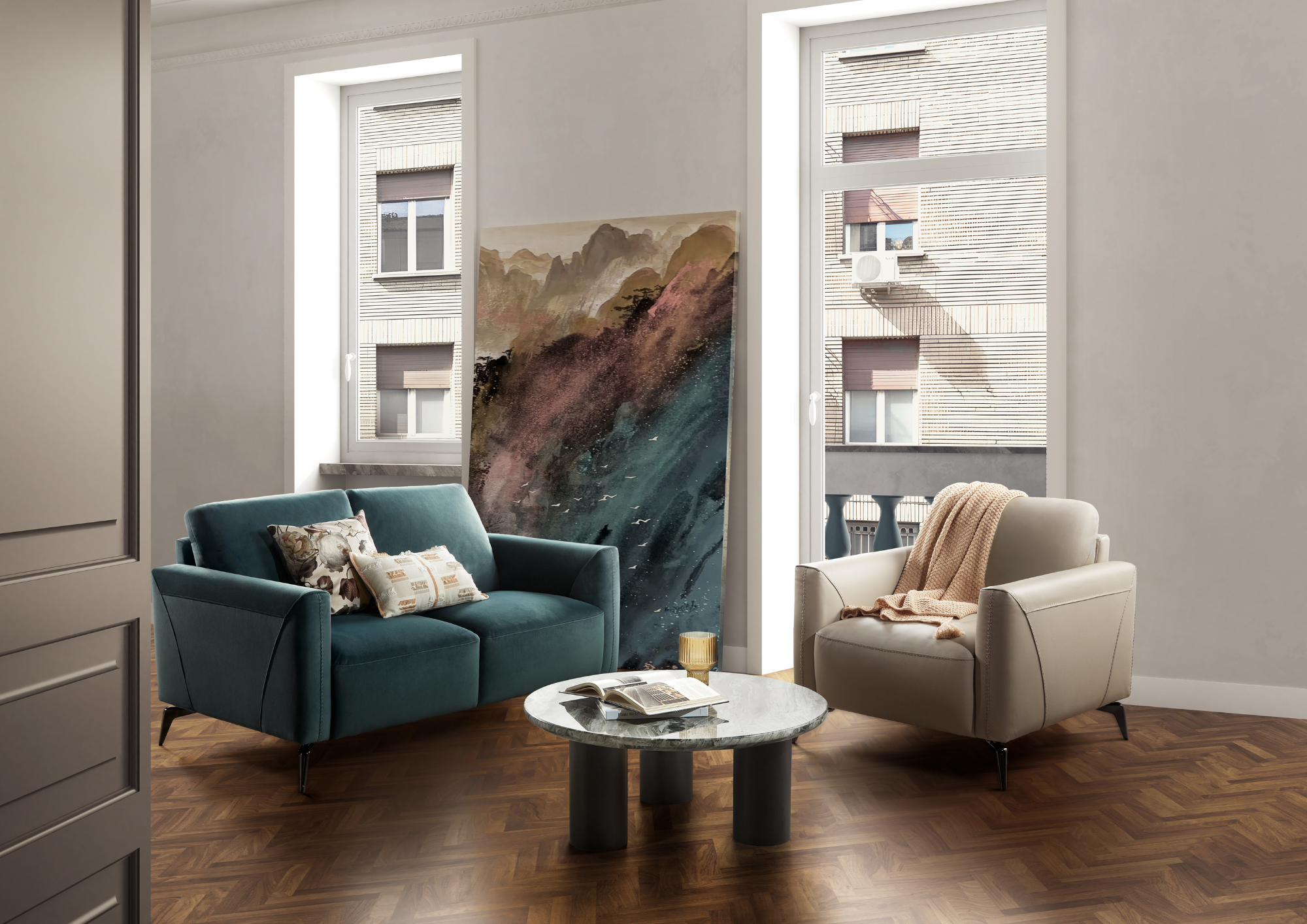 Living room with two armchairs (a teal one with floral pillows and a cream one with a beige throw), a round marble coffee table with a magazine, and large windows showing neighboring brick buildings.