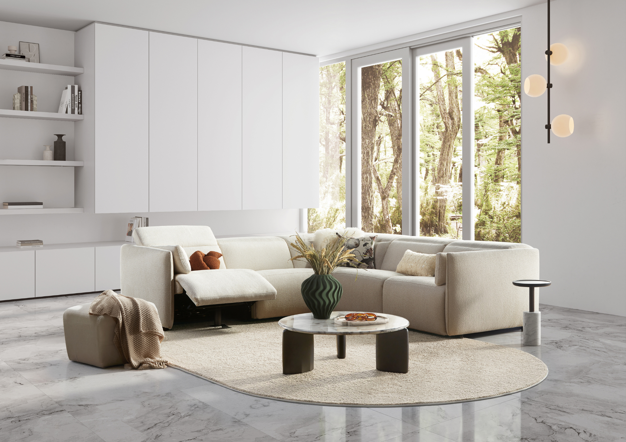 Modern living room with white sectional sofa, round marble coffee table, large window showing trees outside, minimal décor, and a wall-mounted black and beige light fixture.