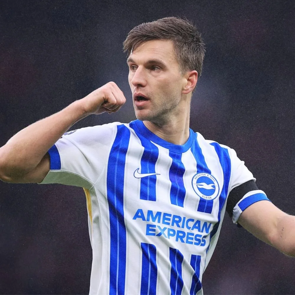A male soccer player in a white and blue striped jersey celebrating with his fist raised and looking to the side.