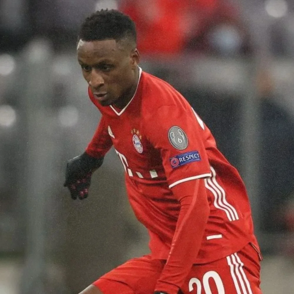 A soccer player from Bayern Munich wearing a red jersey with the number 20, on a rainy field, focusing on the game.
