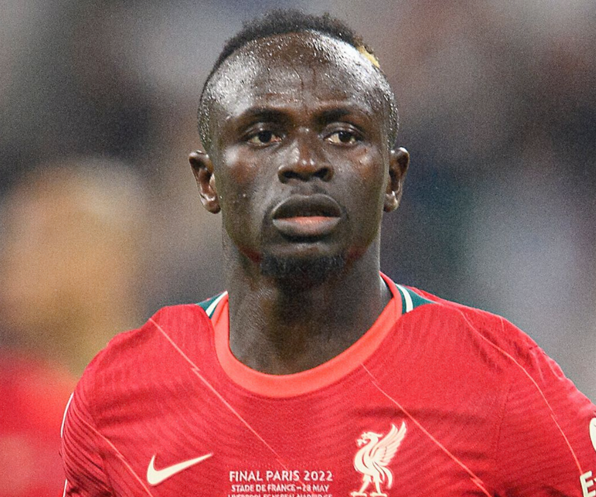 A male soccer player wearing a red Liverpool jersey during a match, with sweat on his face, looking ahead with a serious expression.