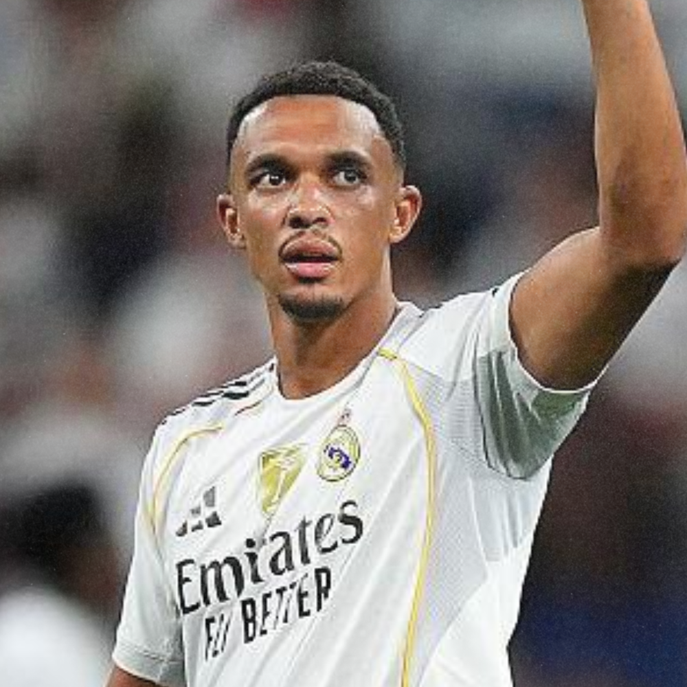 A football player wearing a white jersey with the Real Madrid logo, looking focused and pointing with his right hand during a game.