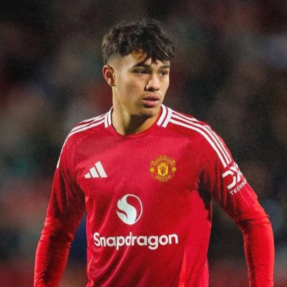 A male soccer player wearing a red Manchester United jersey with the Snapdragon logo, music note emblem, and Adidas stripes on the shoulders.