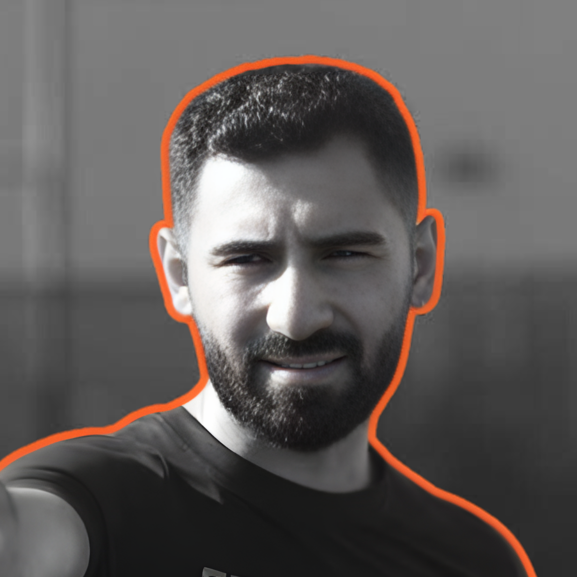 A black and white photo of a man with short dark hair and a beard, wearing a black shirt, with an orange outline around him.