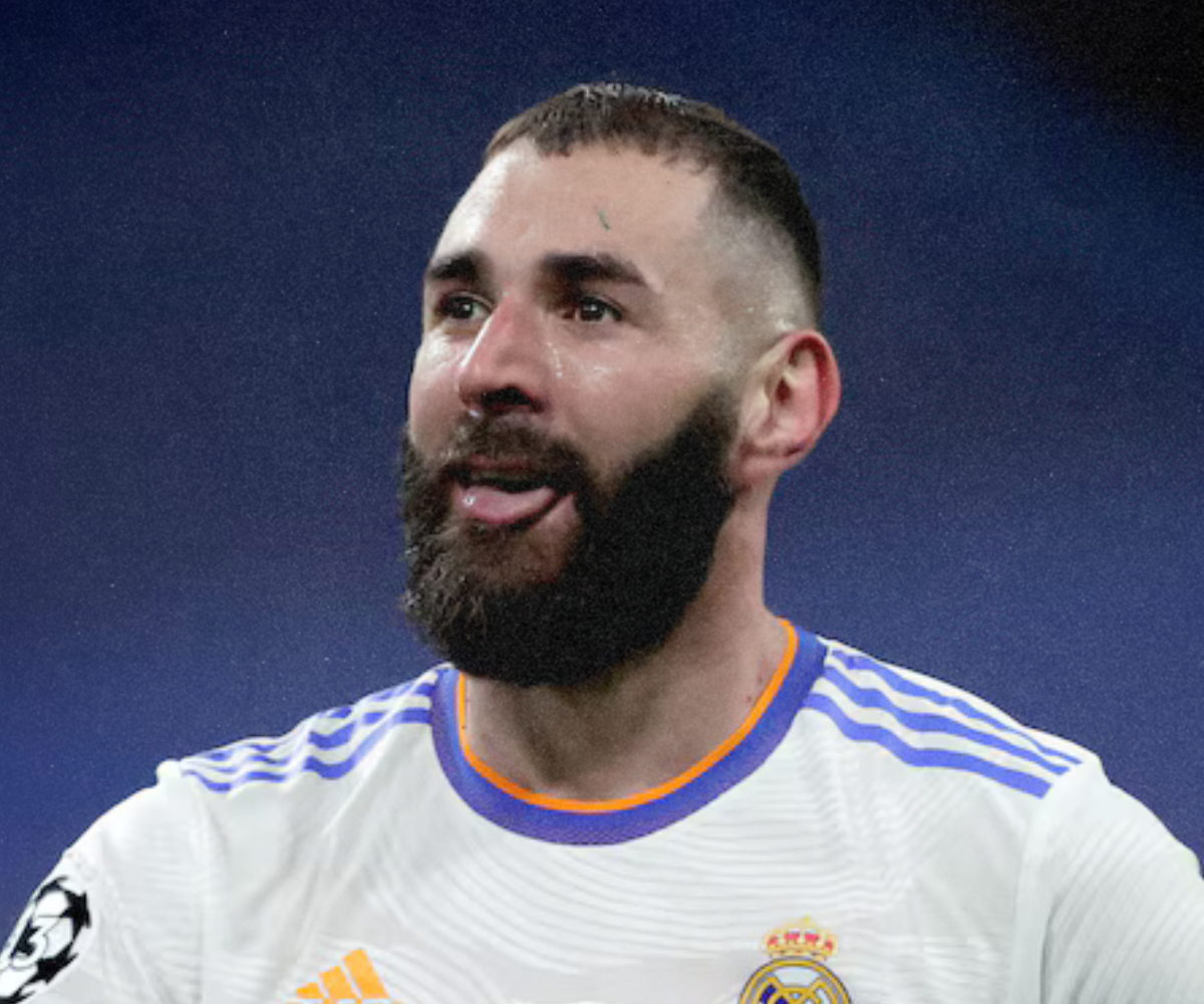Close-up of a male soccer player with a beard, wearing a white Real Madrid jersey, making a playful face with his tongue out during a game.