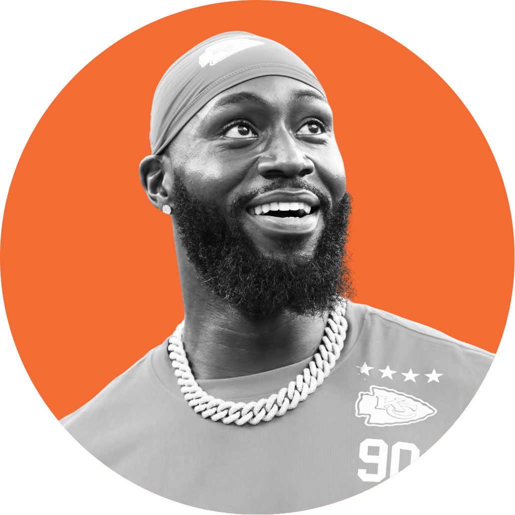 Black and white photo of a smiling man wearing a cap, necklace, and a sports jersey with the Kansas City Chiefs logo and the number 90, set against an orange background.