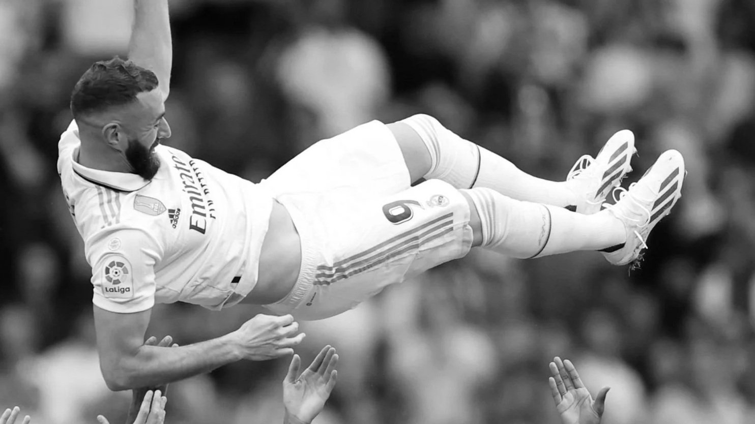 A soccer player with a beard in a jersey with the number 9, being lifted and celebrated by fans in the stands during a match.