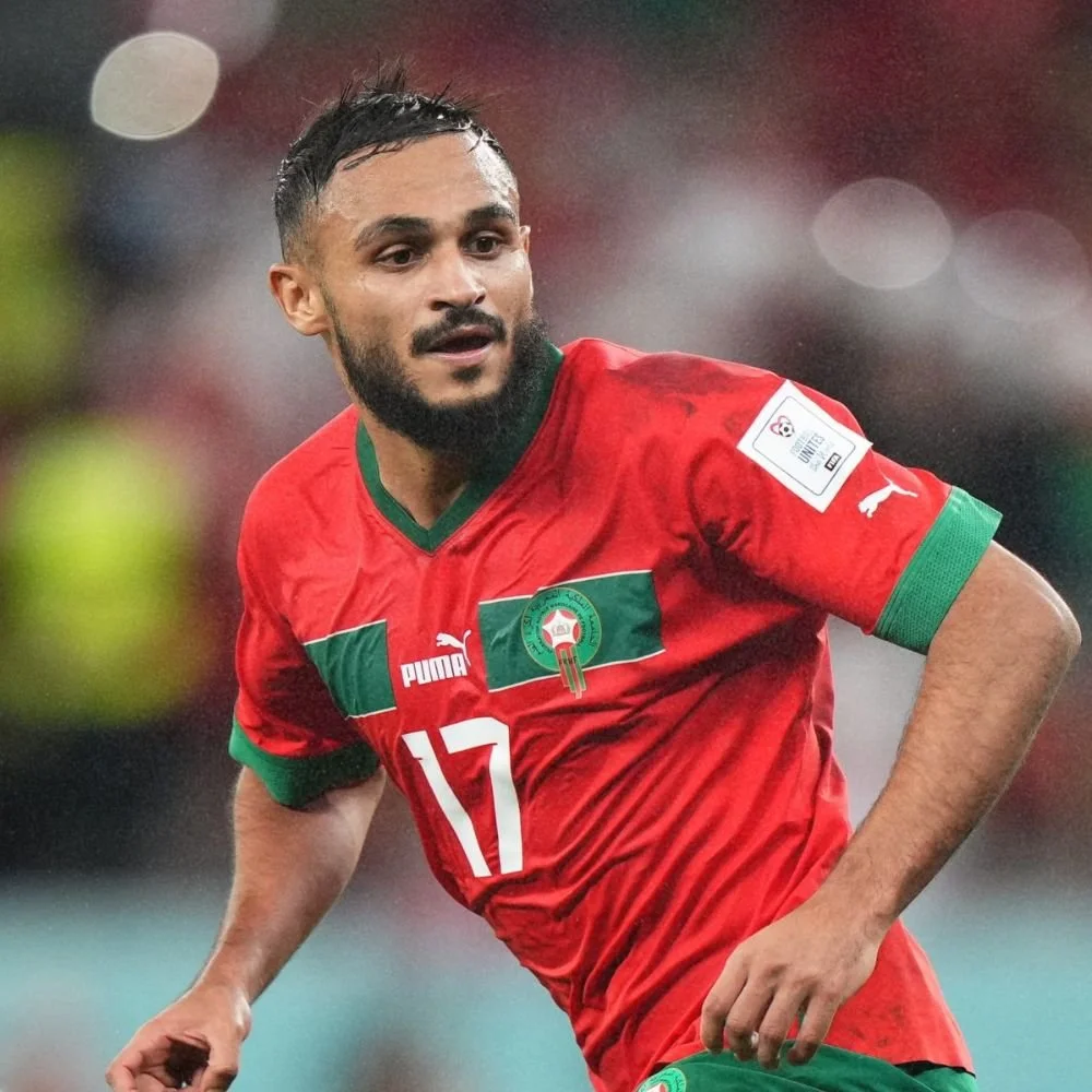 A male soccer player wearing a red uniform with green accents, number 17, on a field during a game under rainy conditions.