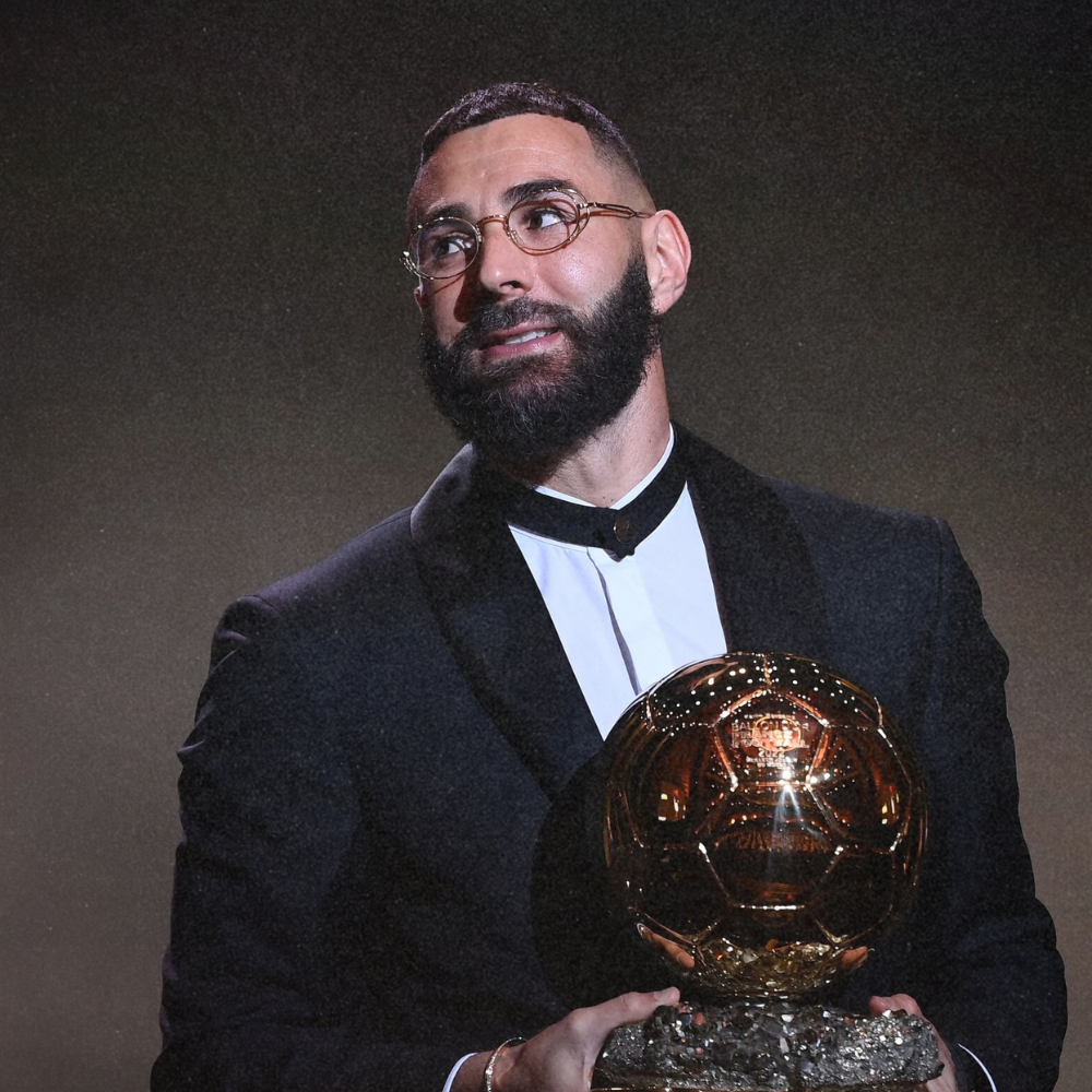 A man dressed in a tuxedo holding a golden soccer ball award.