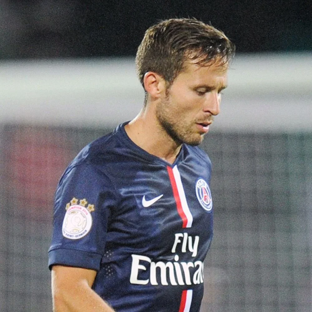 A male soccer player in a dark blue jersey with the Paris Saint-Germain logo, looking down with a serious expression.