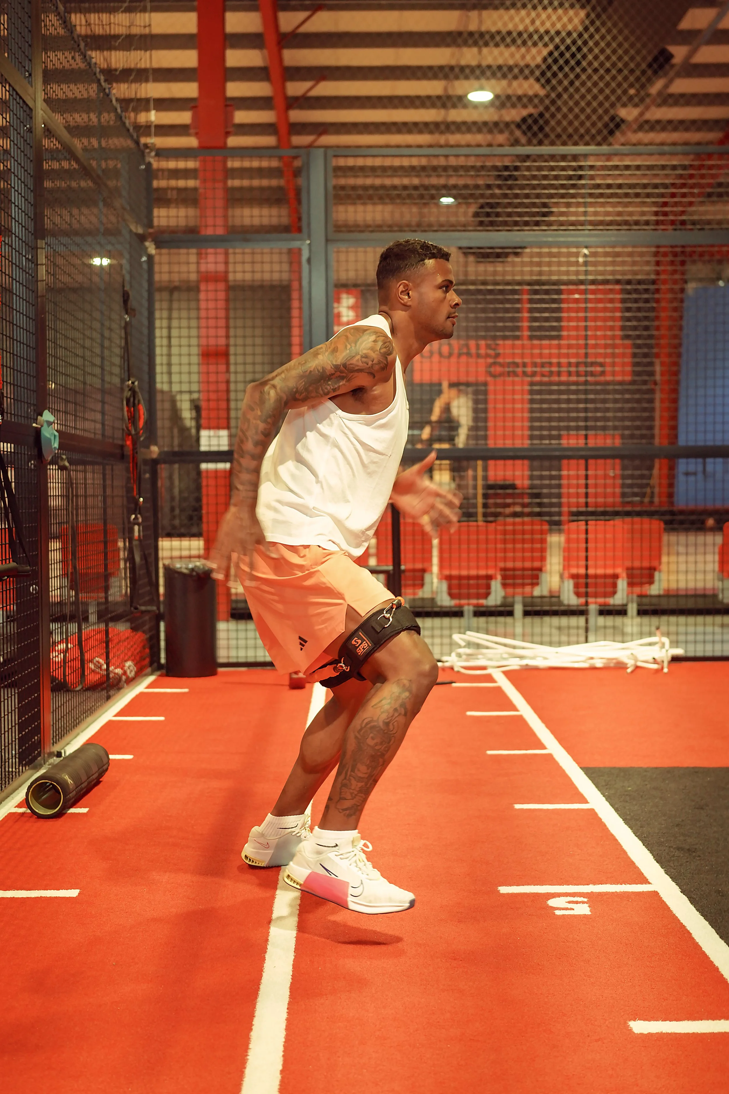 Man in athletic wear performing a sprint start on a track in an indoor gym.