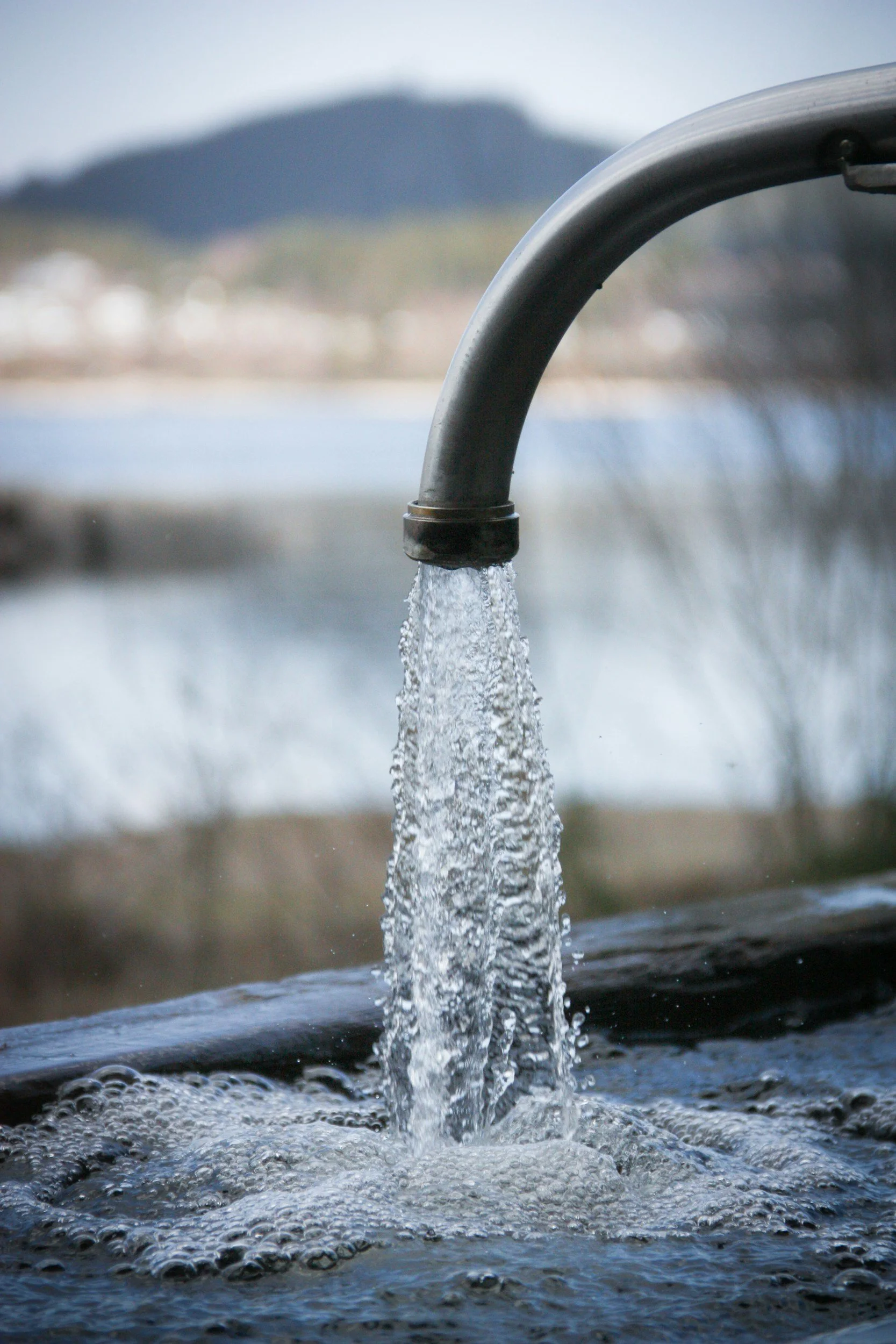 Close-up of a metal water pipe with water flowing out into a pool.