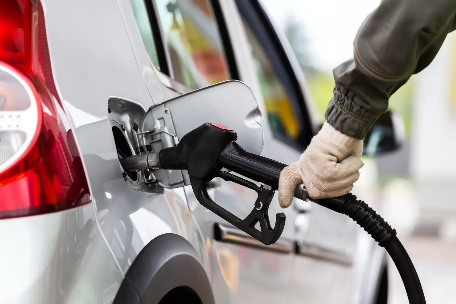 Close-up of a person refueling a silver SUV at a gas station with a black fuel nozzle.