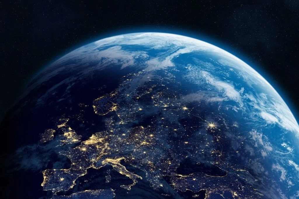 Earth seen from space at night, showing illuminated cities and landmasses across Europe and parts of Asia.