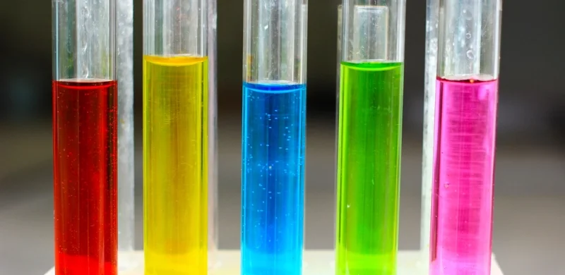 Test tubes filled with colorful liquids in red, yellow, blue, green, and pink, on a laboratory table.