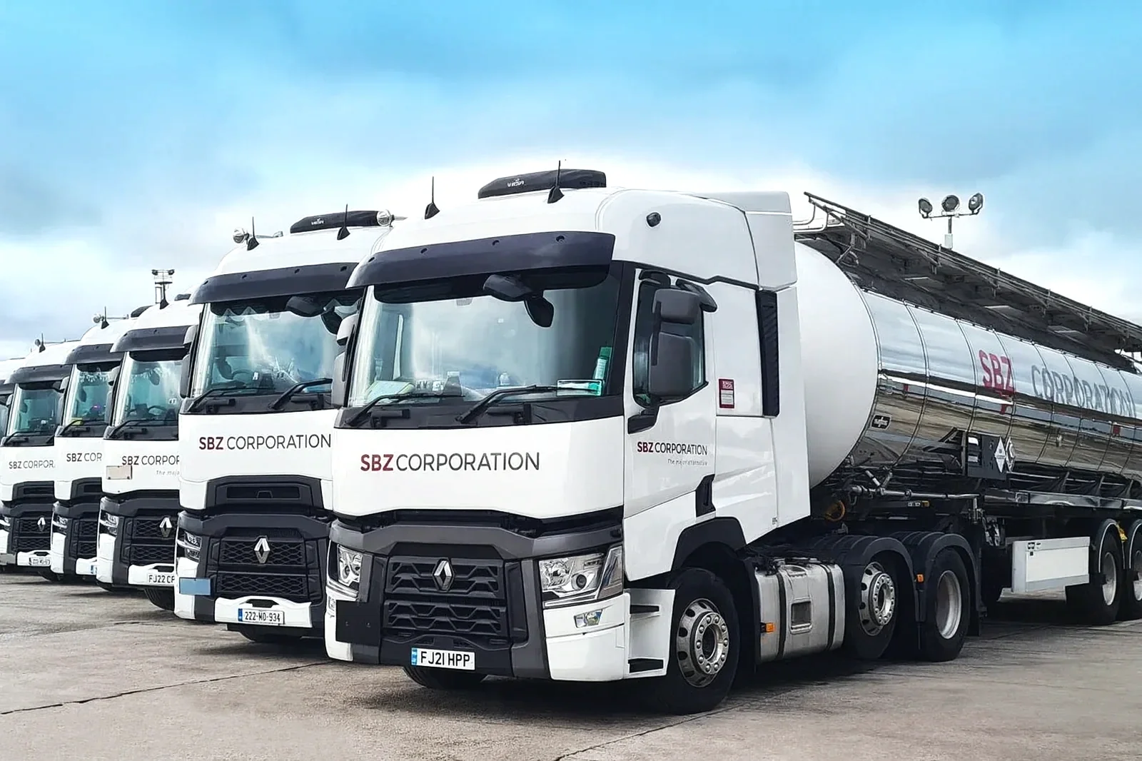 Line of white SBZ tanker trucks parked side by side on a concrete lot.