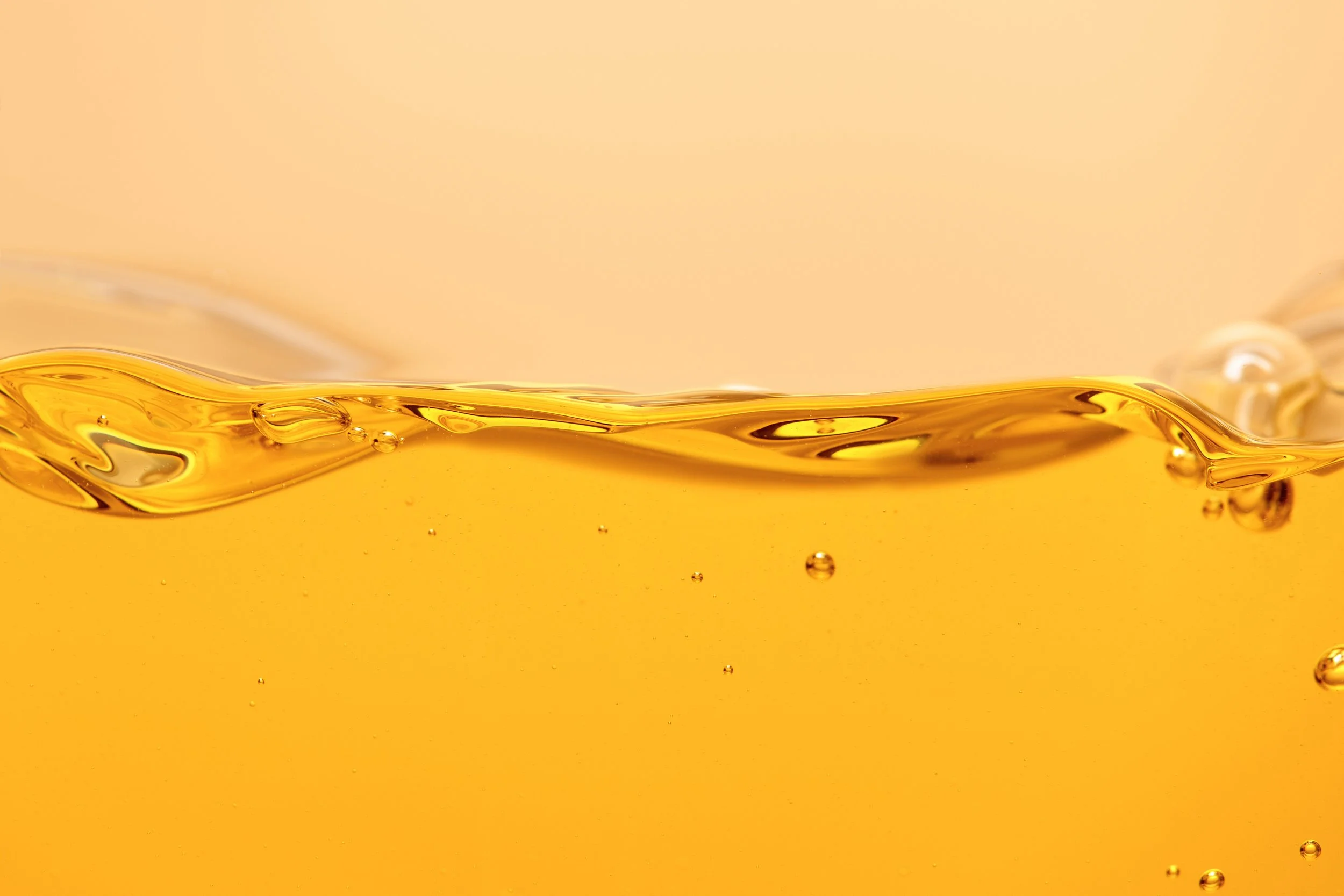 Close-up of golden liquid, possibly oil or honey, with visible bubbles and ripples.