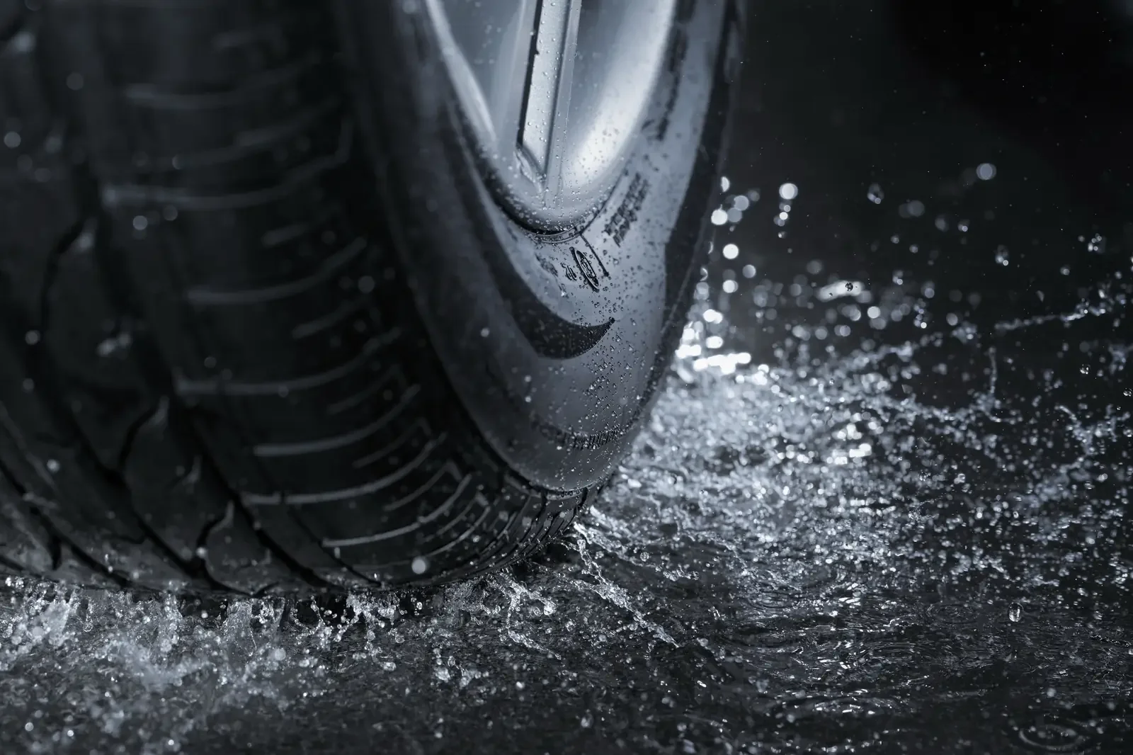 Close-up of a car wheel driving through water with water spraying around the tire.