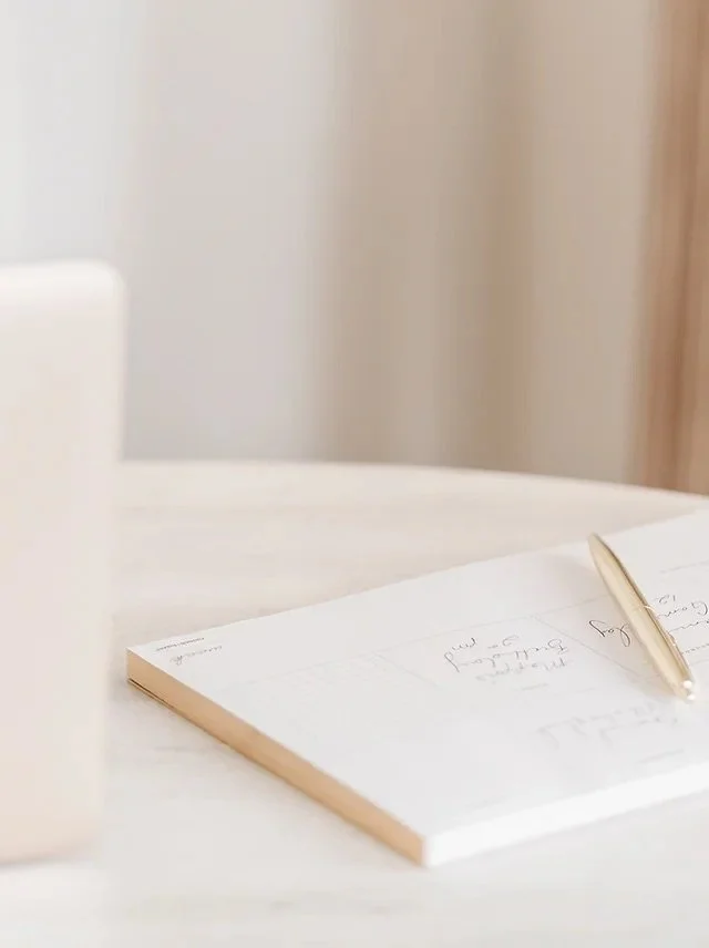 A close-up of a white desk with a notebook and a pen placed on it.
