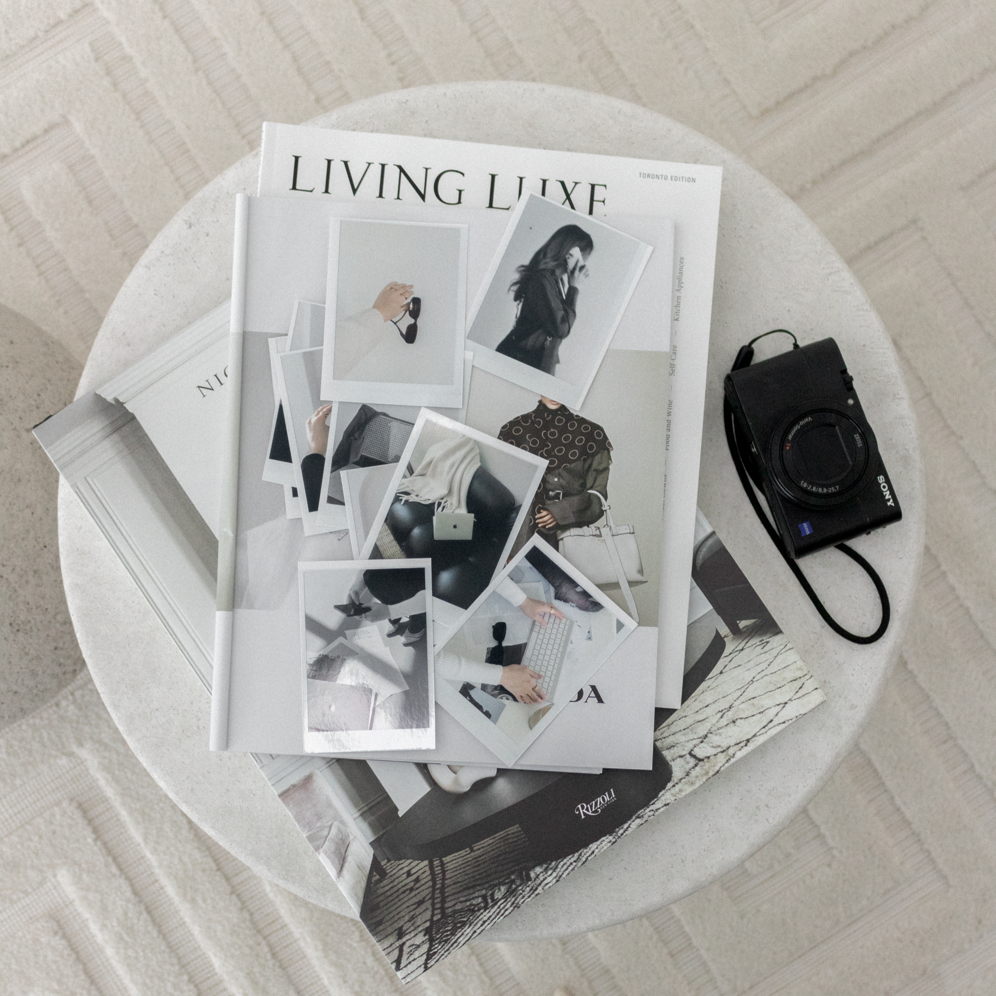 A small round table with magazines, instant photos, and a Sony digital camera placed on top.