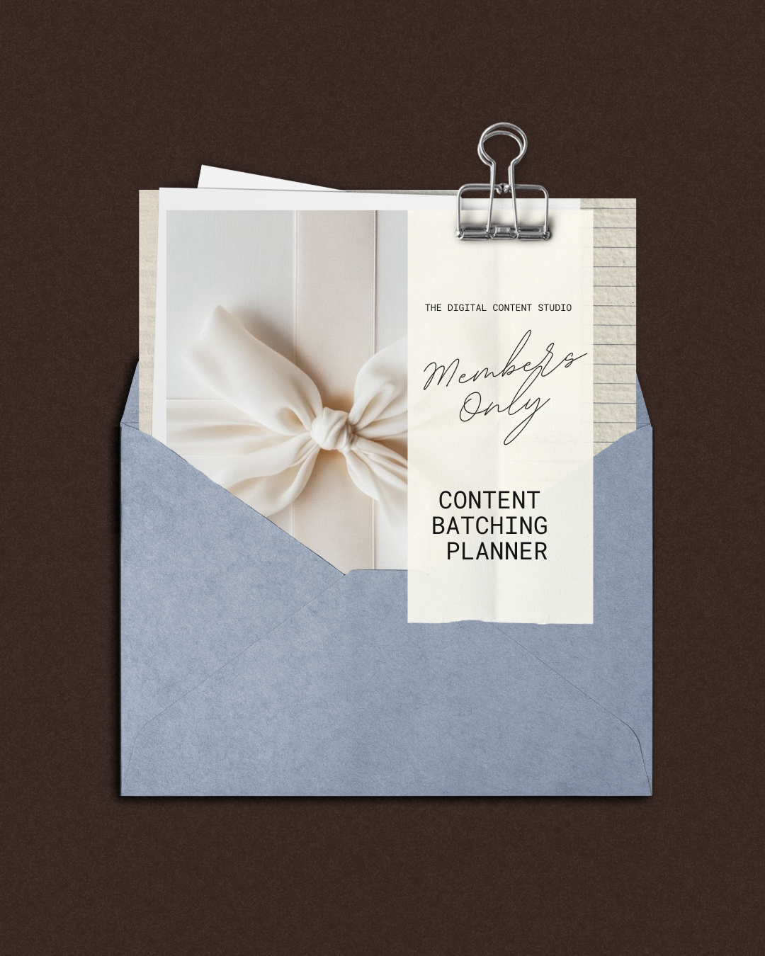 An envelope containing a content batching planner with a white bow, clipped with a paper clip, on a dark surface.