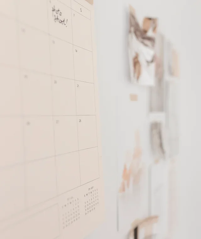 A large wall calendar with some handwritten notes, alongside various photos and notes pinned to the wall.