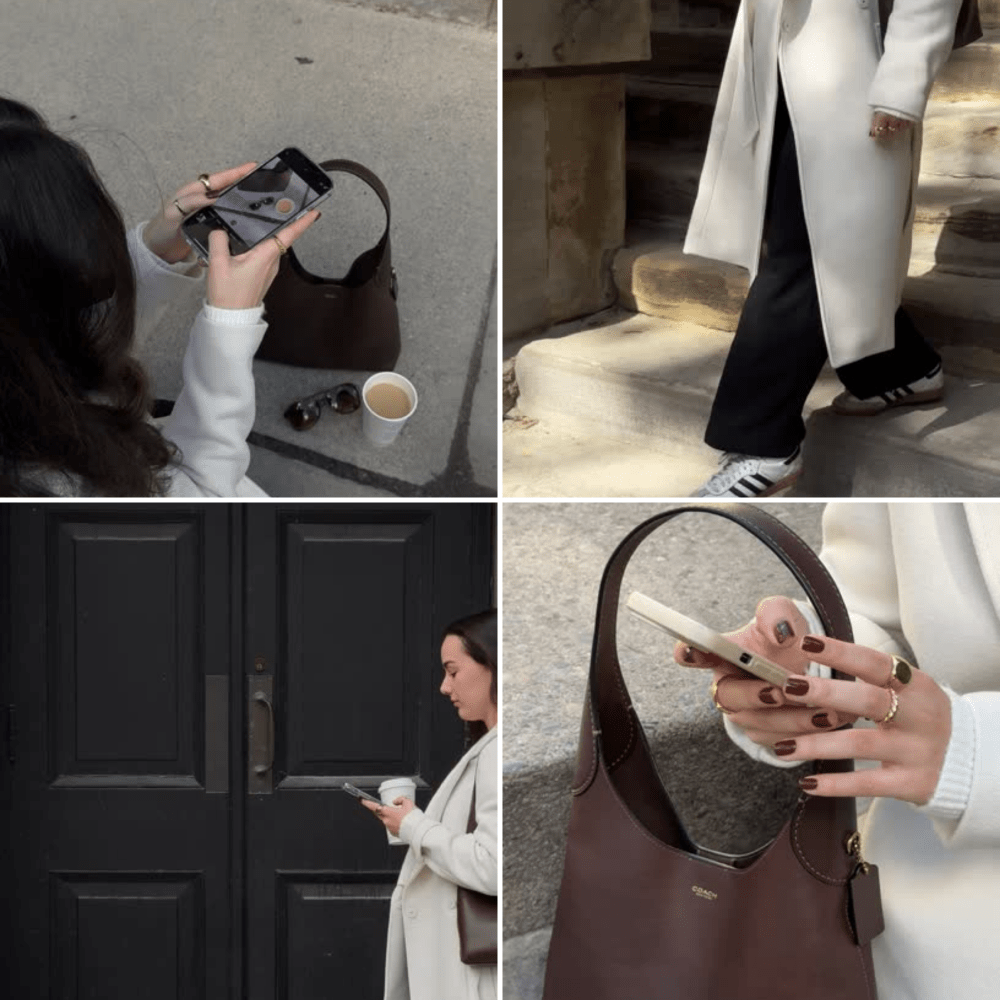 A woman in a white coat and dark pants using her phone outside, with a brown purse and sunglasses on the ground beside her. She stands in front of a black door, also looking at her phone.