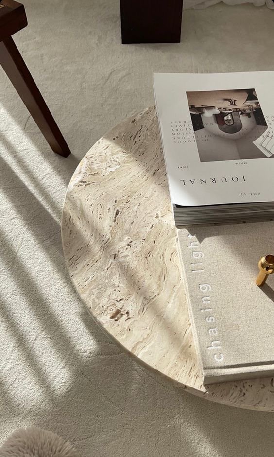 Close-up of a round marble coffee table with books and a small golden decorative object on it, located on a light-colored carpet.