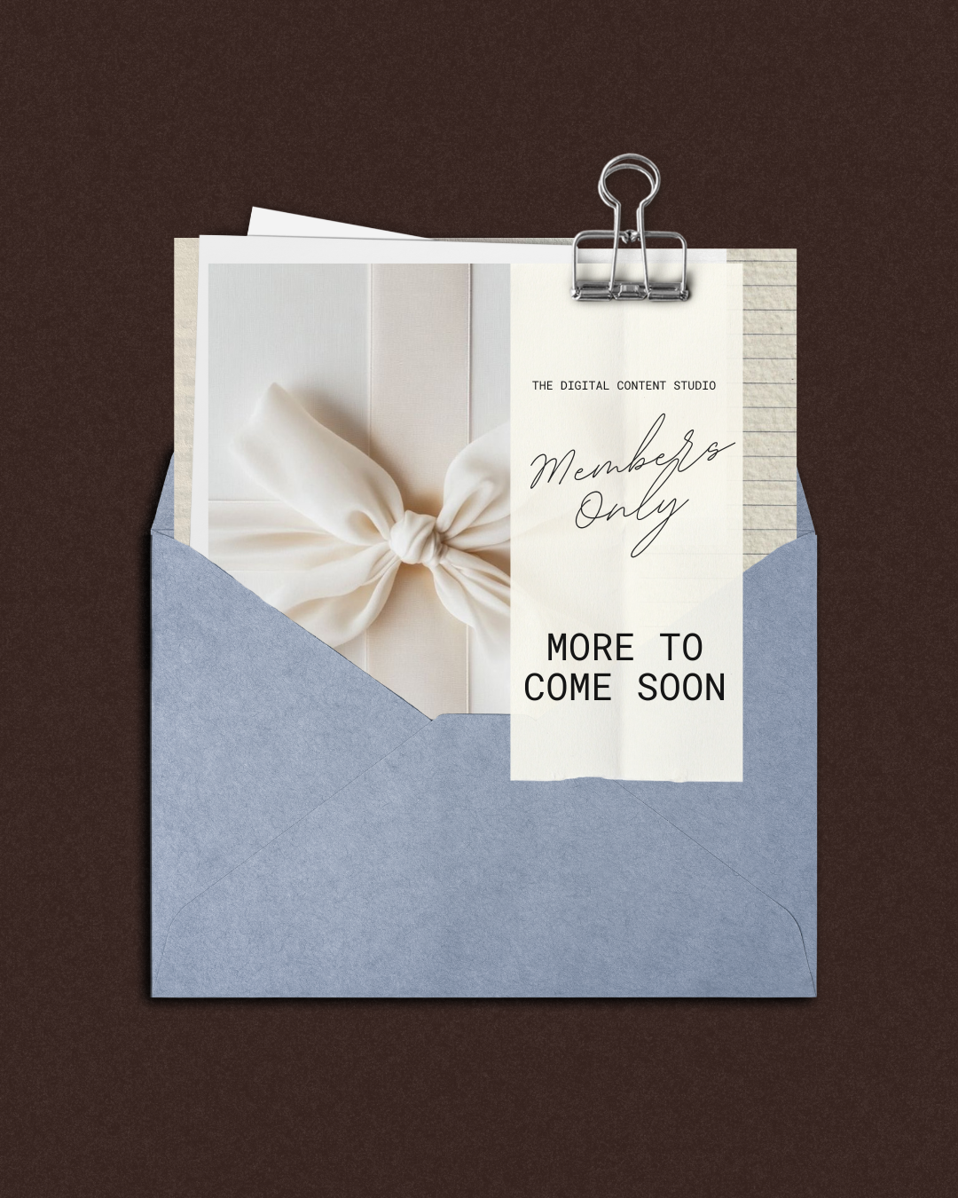 A blue envelope partially open with a white card inside, displaying a cream-colored satin ribbon tied in a bow. Attached is a torn piece of paper with the words 'Members Only' and 'More to Come Soon' printed on it, held by a silver binder clip.