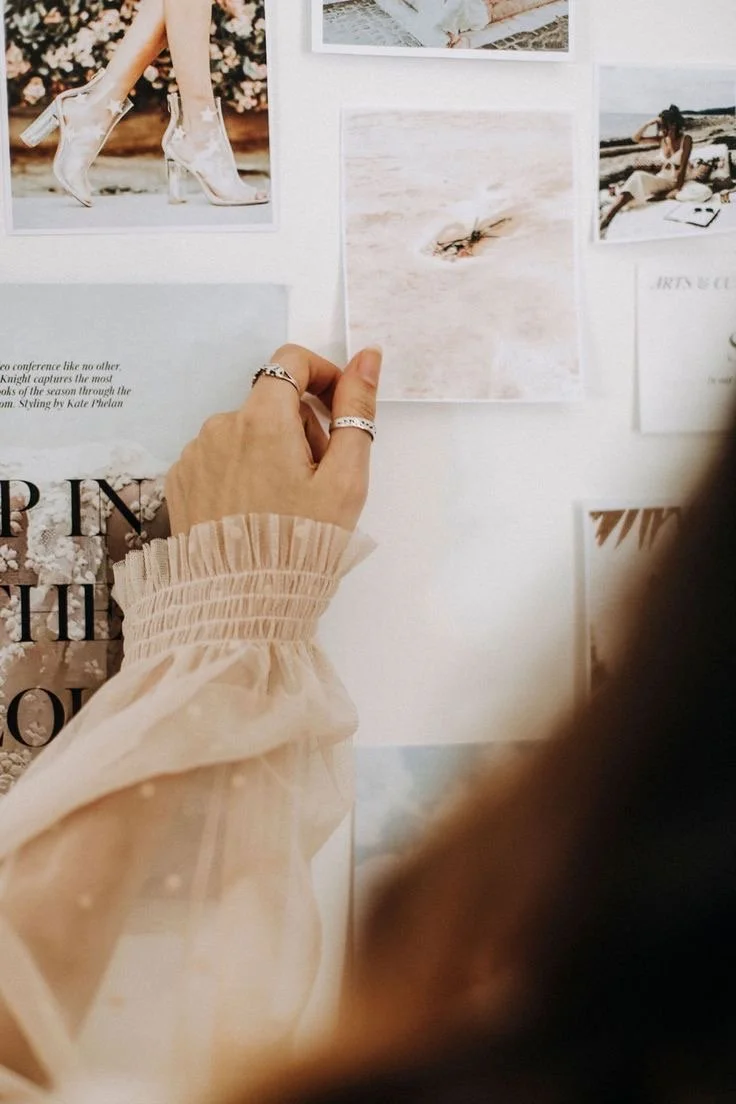 Person adjusts a photo on a wall featuring beach and fashion images.