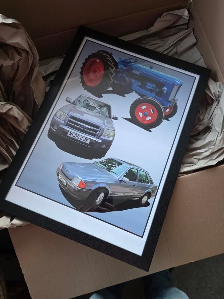 Framed illustration of two cars and a tractor, with a background of crumpled paper and a cardboard box.