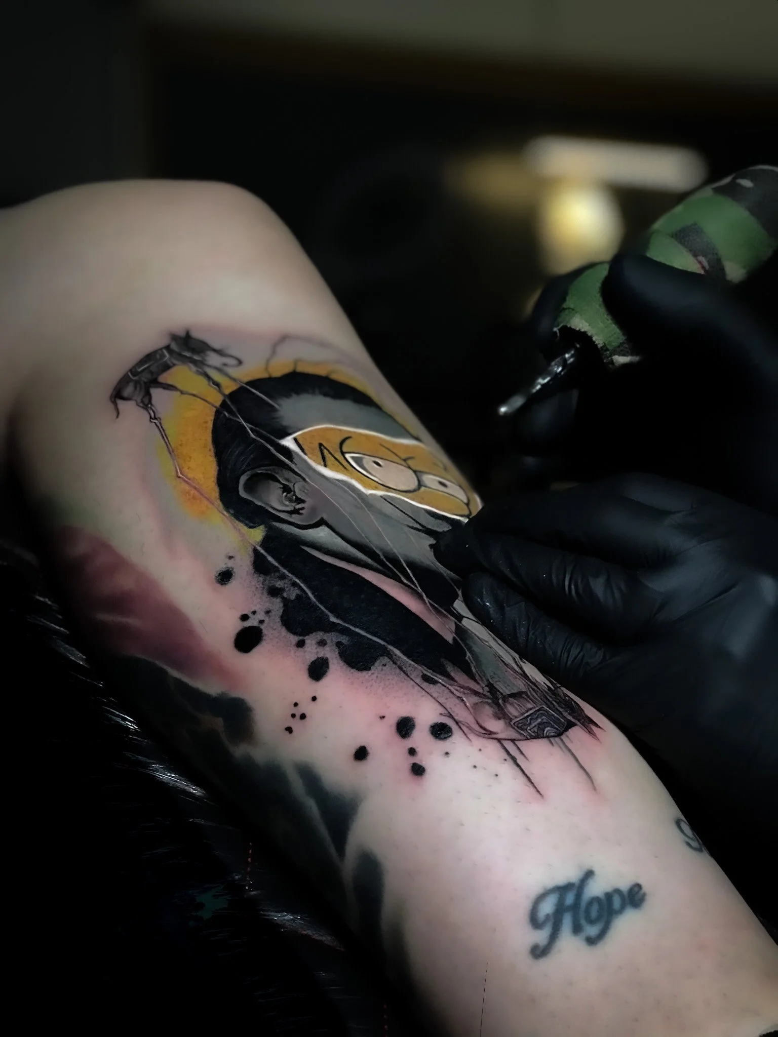 A person getting a colorful tattoo on their arm, including a portrait and the word 'Hope' written in cursive, with black ink and some shading.