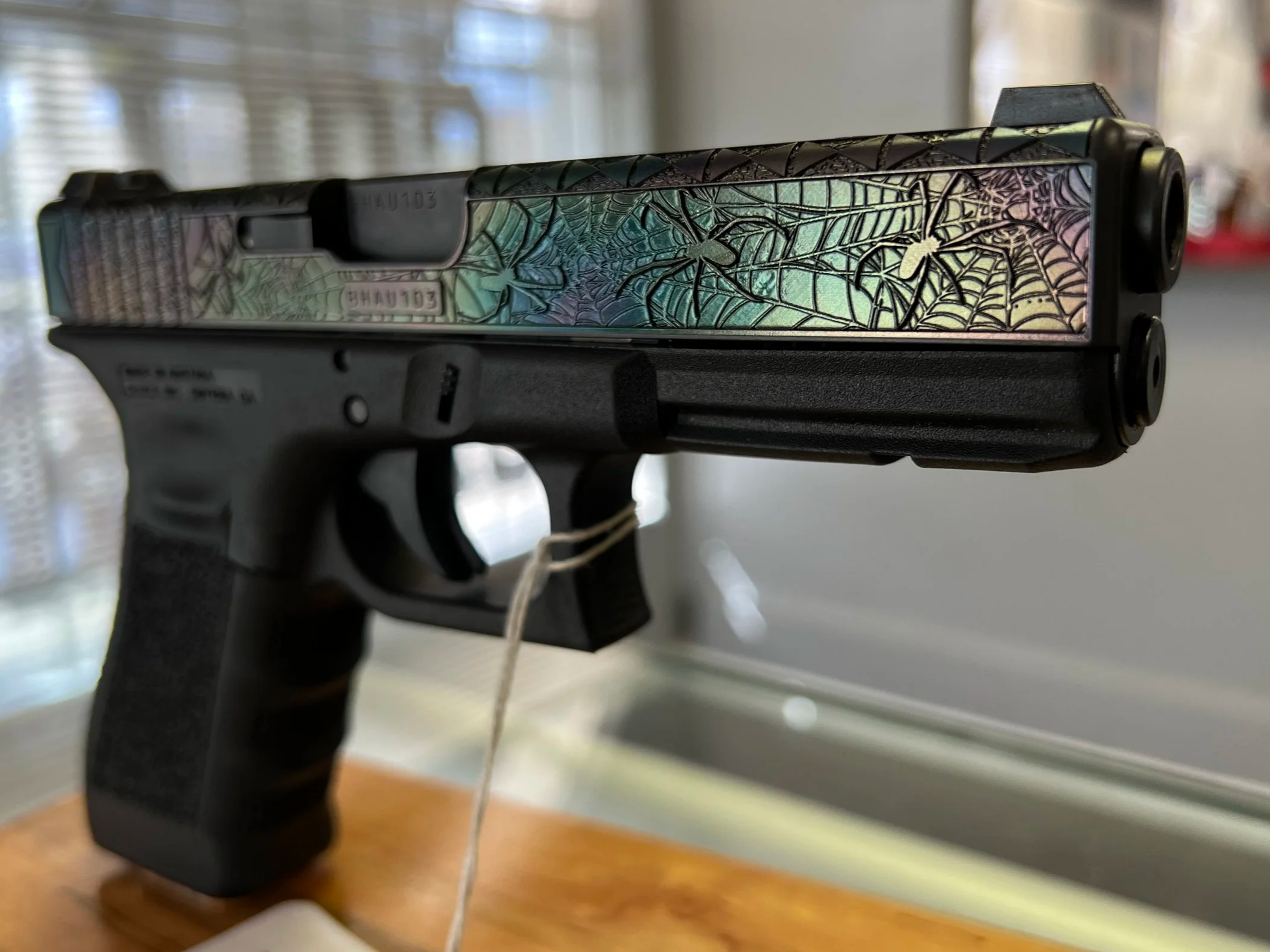 Custom Glock® 17 featuring spider web–inspired slide engraving with an iridescent finish and a black hand-stippled frame, showcasing detailed craftsmanship and personalized design work.