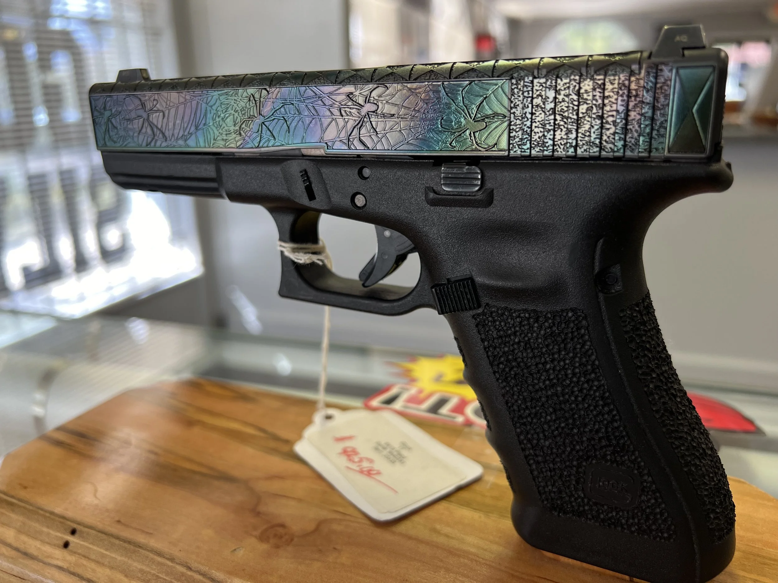 Custom Glock® 17 featuring spider web–inspired slide engraving with an iridescent finish and a black hand-stippled frame, showcasing detailed craftsmanship and personalized design work.