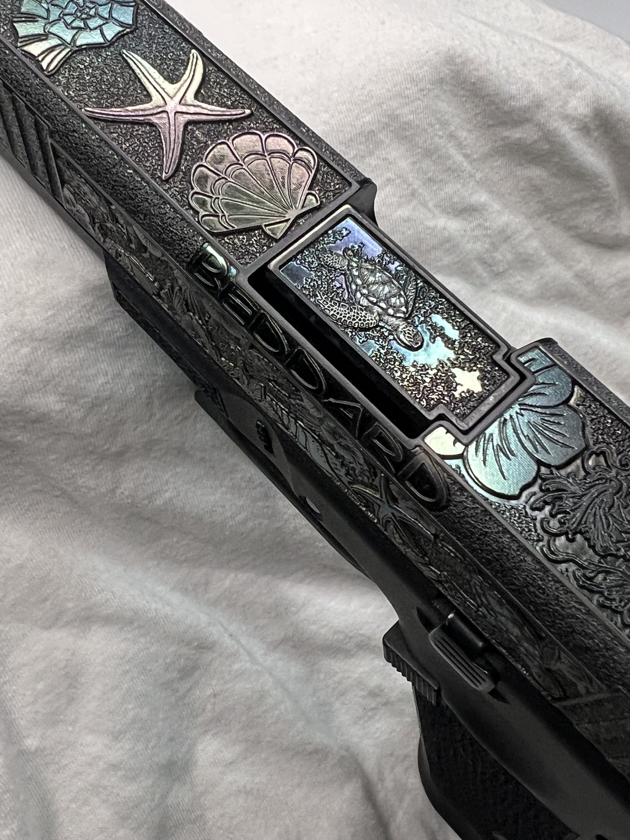 Custom Glock® 40 featuring decorative ocean scene slide engraving with colorful etched artwork and a black hand-stippled frame, showcasing detailed craftsmanship and personalized design work.