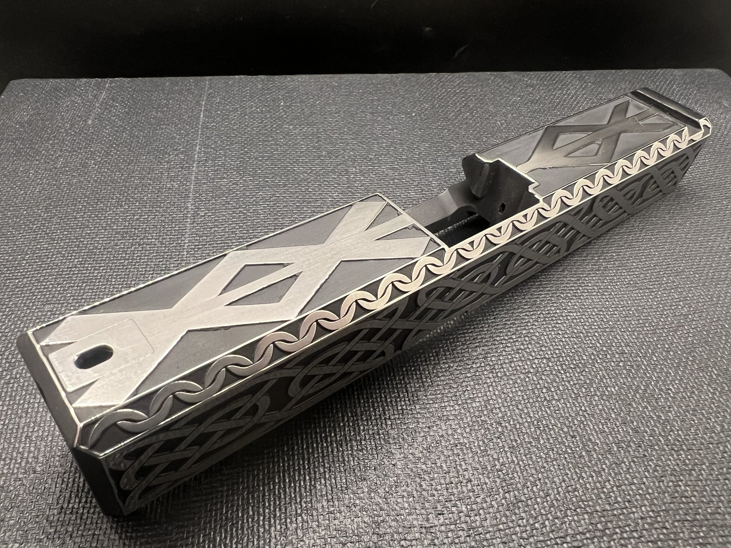 Custom engraved firearm slide featuring detailed Celtic knot pattern engraving with a dark Cerakote finish, showcasing precision laser craftsmanship.