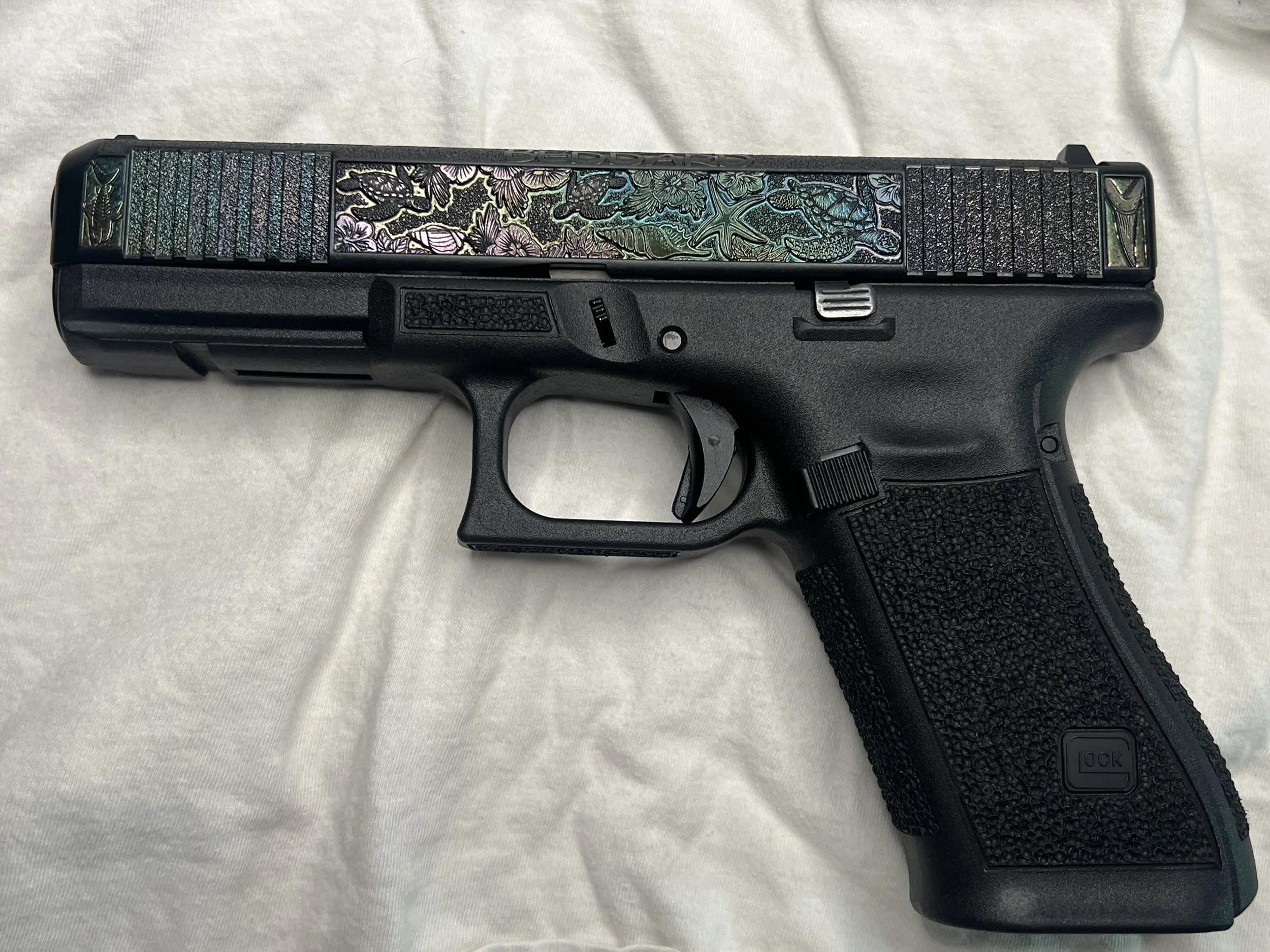 Custom Glock® 40 featuring decorative ocean scene slide engraving with colorful etched artwork and a black hand-stippled frame, showcasing detailed craftsmanship and personalized design work.