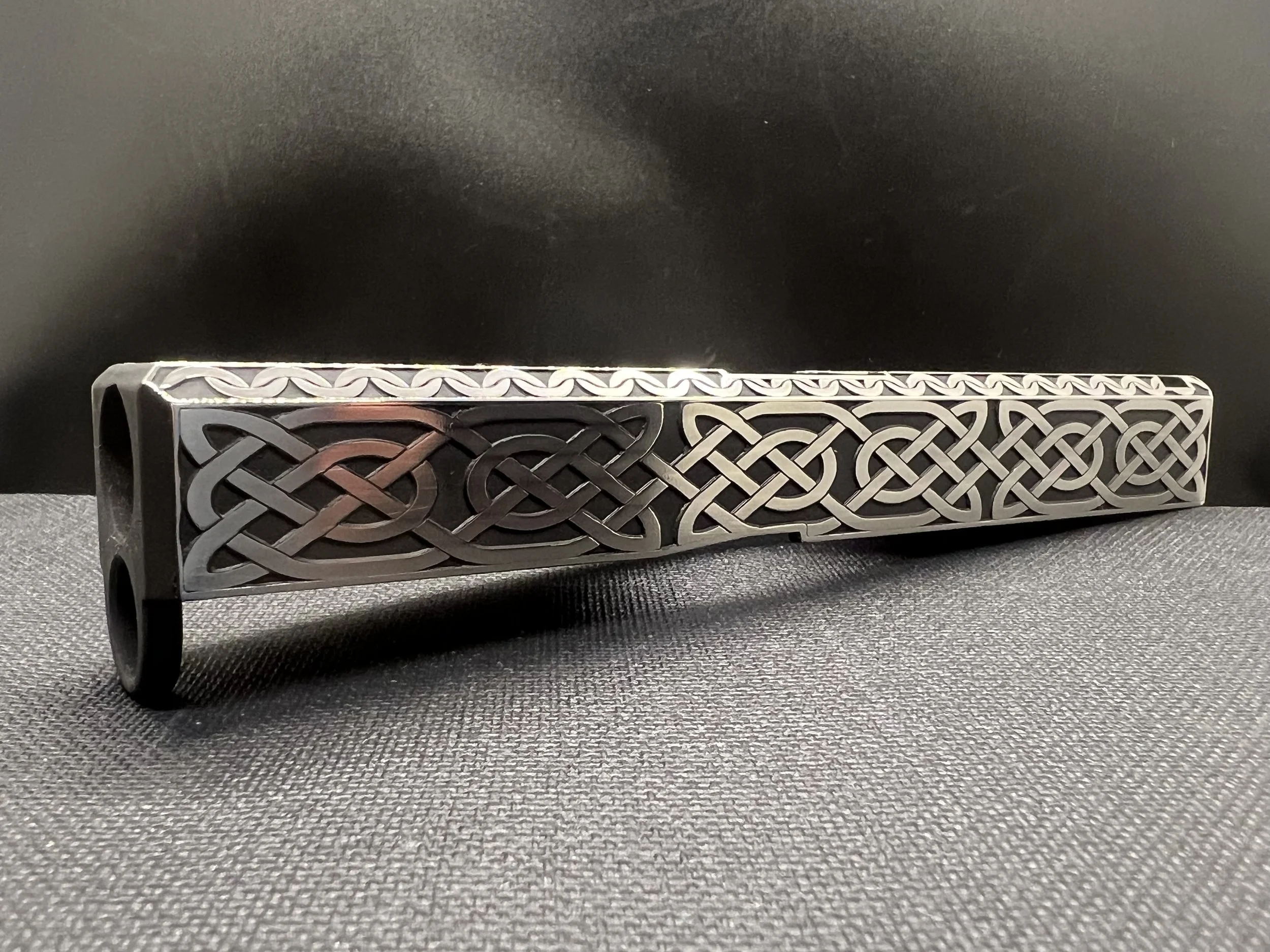 Custom engraved firearm slide featuring detailed Celtic knot pattern engraving with a dark Cerakote finish, showcasing precision laser craftsmanship.
