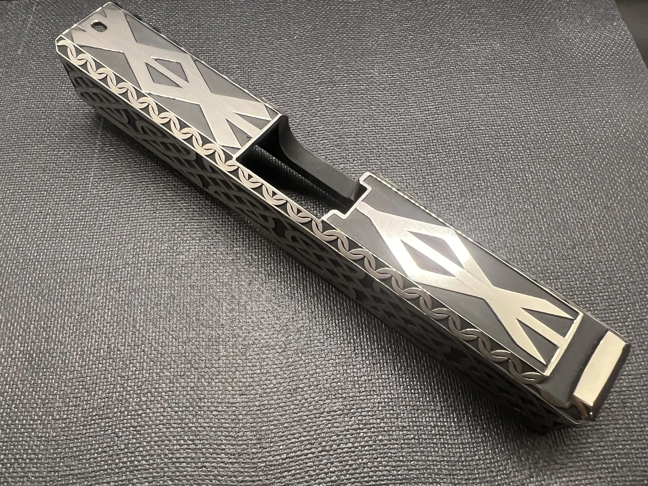 Custom engraved firearm slide featuring detailed Celtic knot pattern engraving with a dark Cerakote finish, showcasing precision laser craftsmanship.