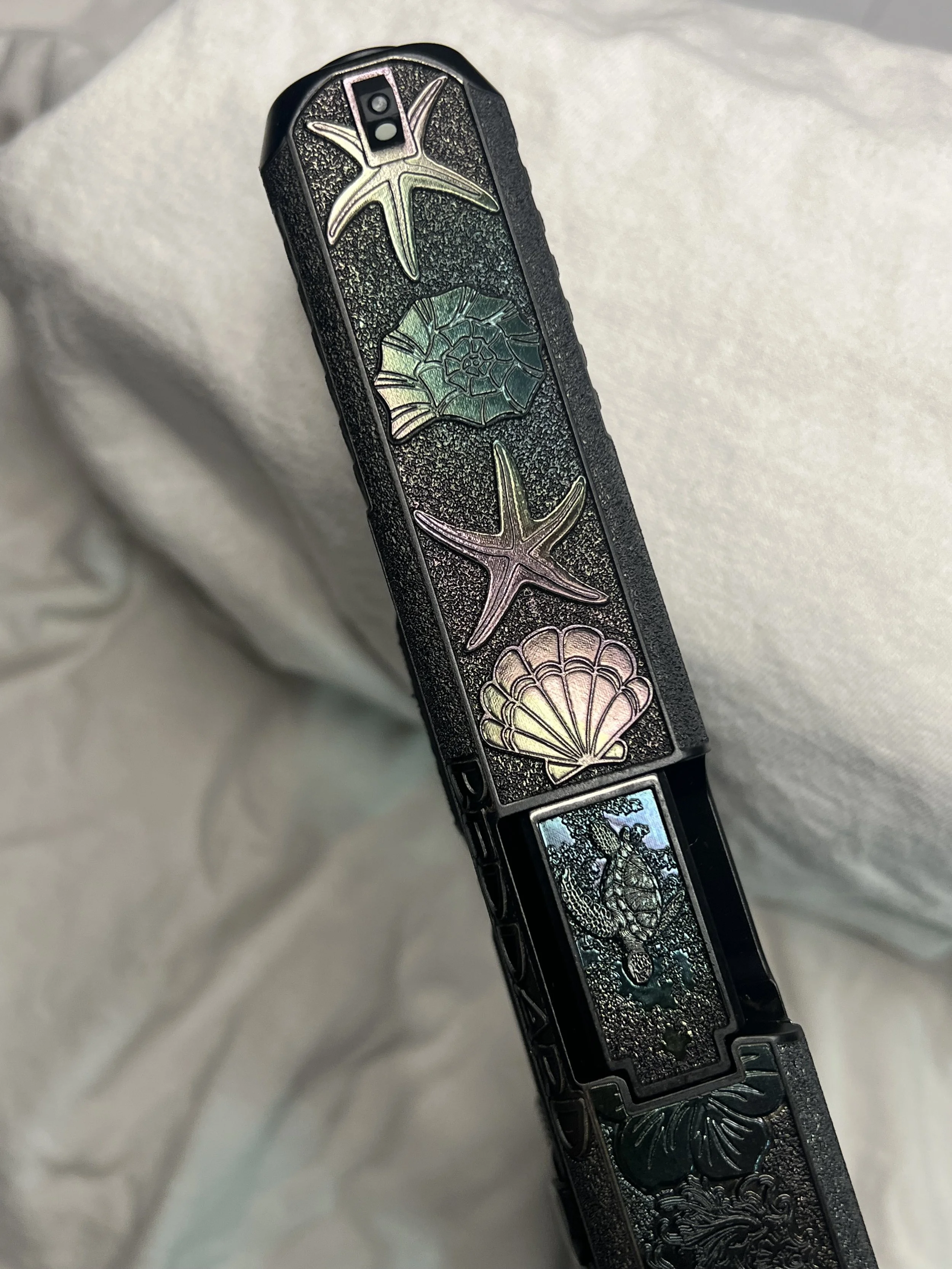 Custom Glock® 40 featuring decorative ocean scene slide engraving with colorful etched artwork and a black hand-stippled frame, showcasing detailed craftsmanship and personalized design work.