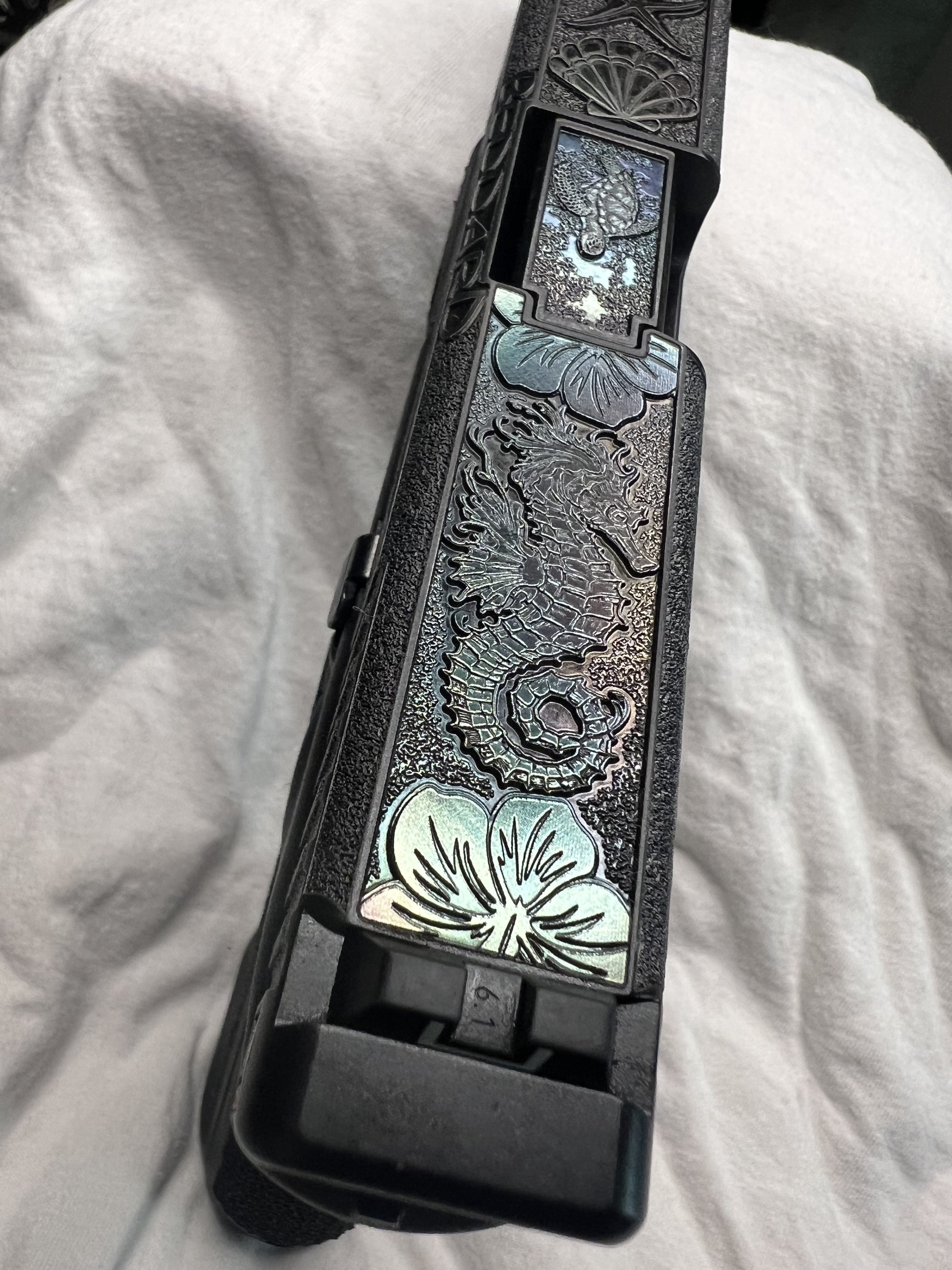 Custom Glock® 40 featuring decorative ocean scene slide engraving with colorful etched artwork and a black hand-stippled frame, showcasing detailed craftsmanship and personalized design work.